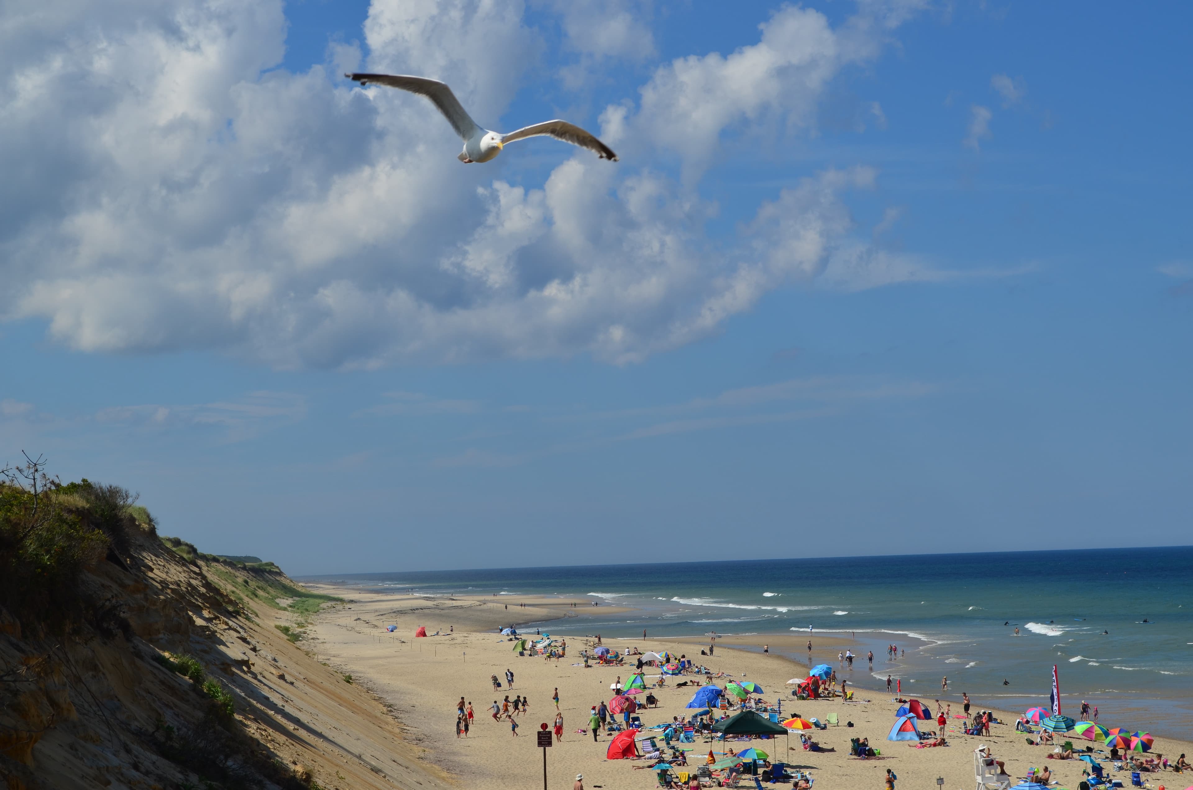 A crowd of people enjoy a wide sandy beach under light clouds and a blue sky.