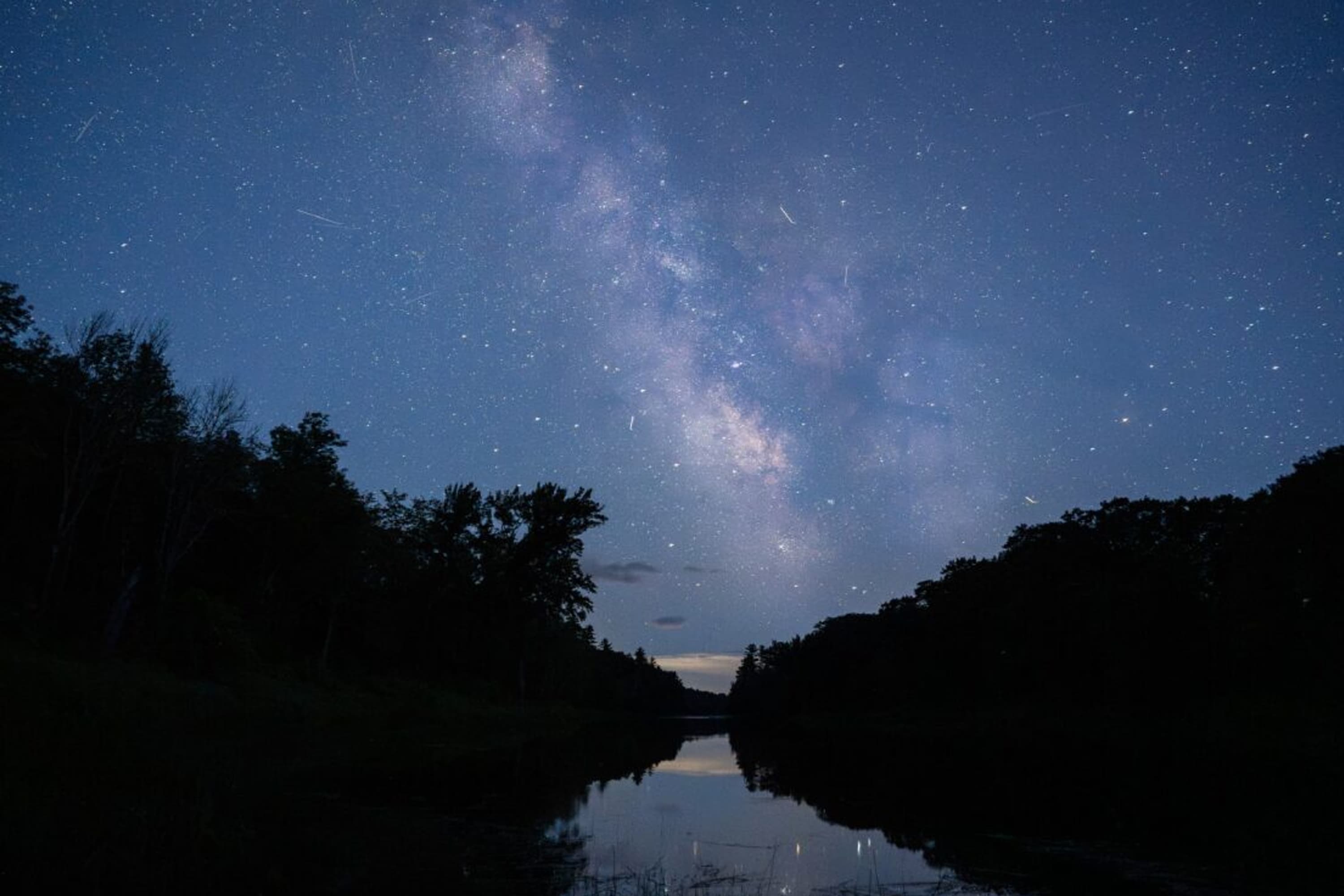 The Milky Way and many stars illuminate the night sky over the river.