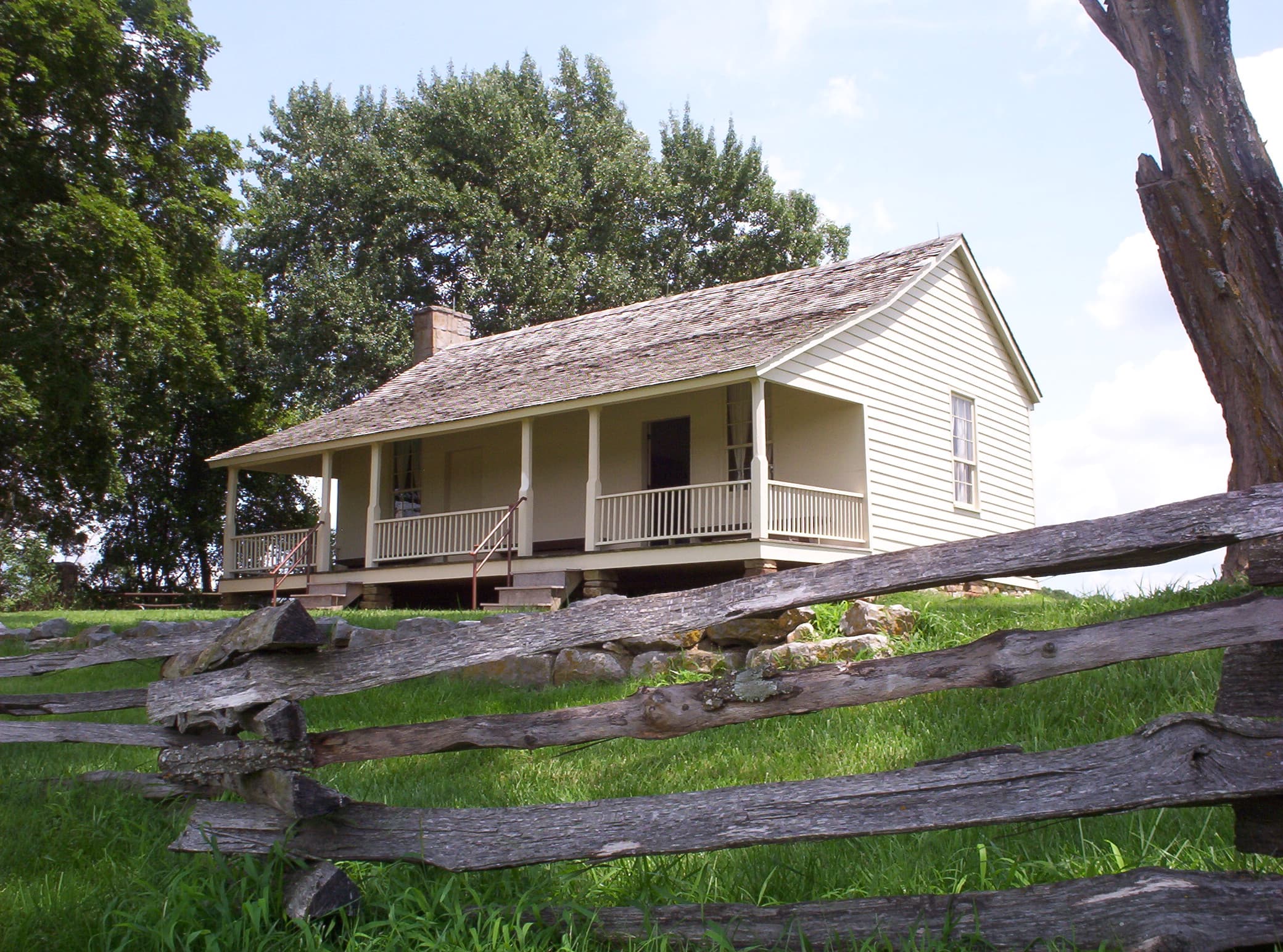 Ray House in the summer with split rail fencing at the border of yard in front of wire road path