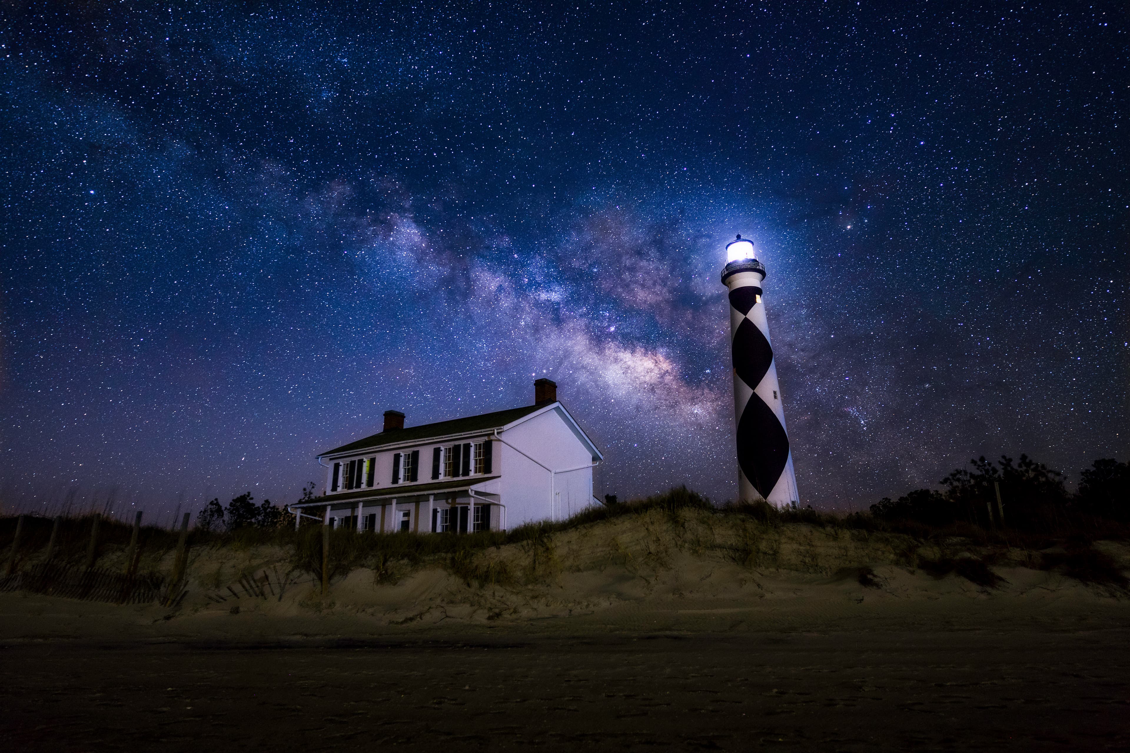 The Milky Way arches across the night sky above the Cape Lookout Lighthouse and Keepers' Quarters
