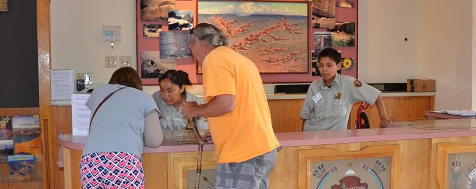Two people in front of a desk and two uniformed people stand behind it.