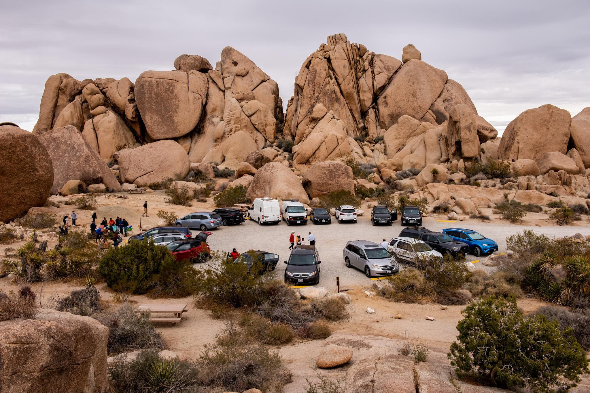 17 cars are parking in a circular dirt lot, numerous people are walking in and around the lot.