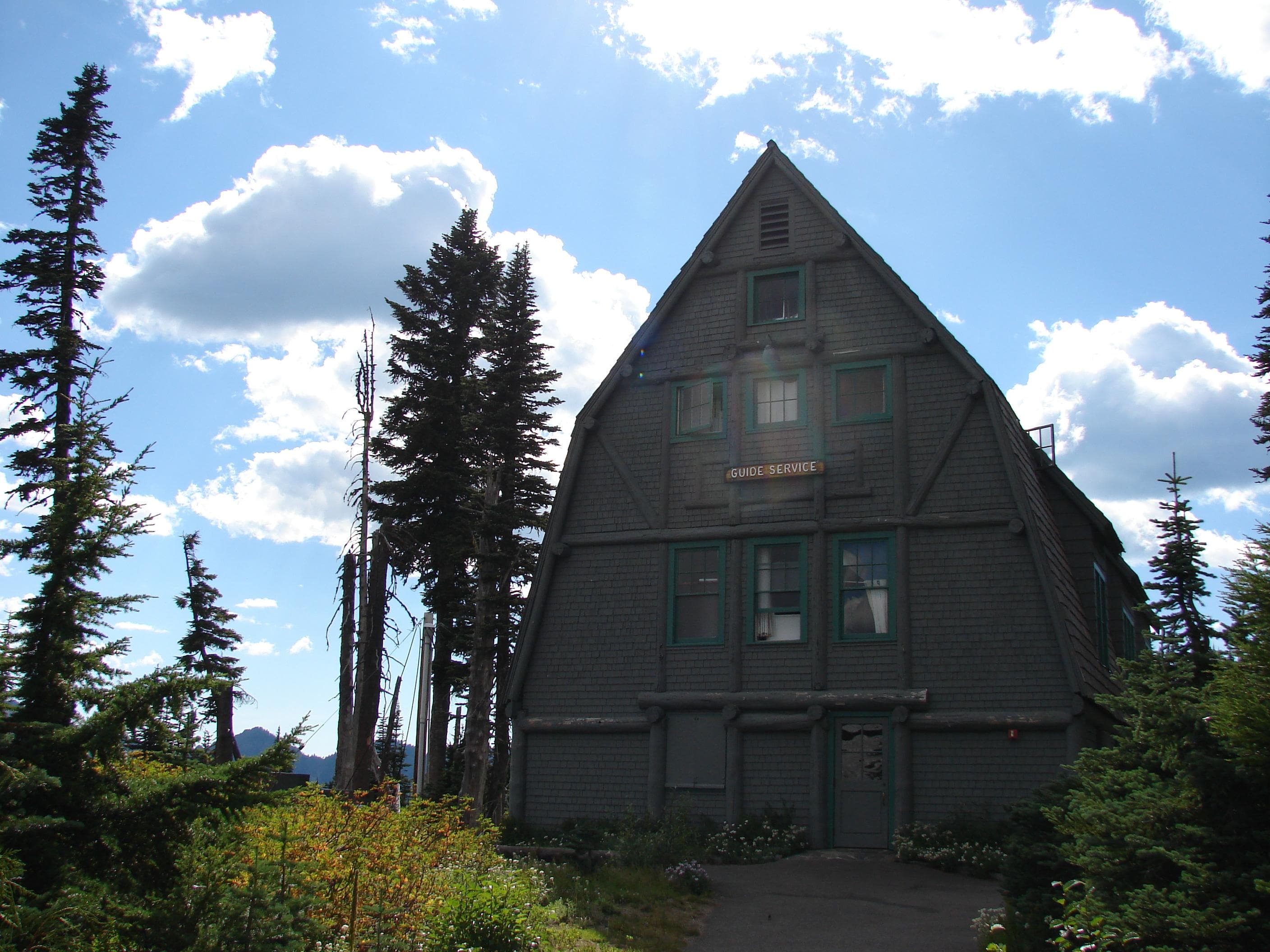 A grey building with sharply-angled roof sits surrounded by trees under a sky dotted with clouds.