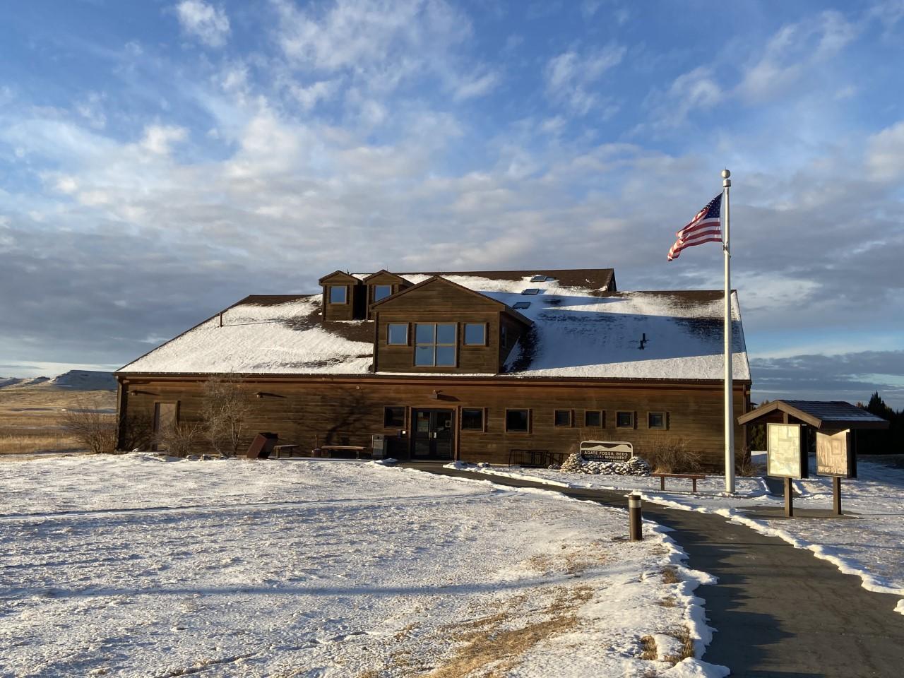 A brown, 2-story building dusted with snow. A path leads leads to the front door and a flag pole.