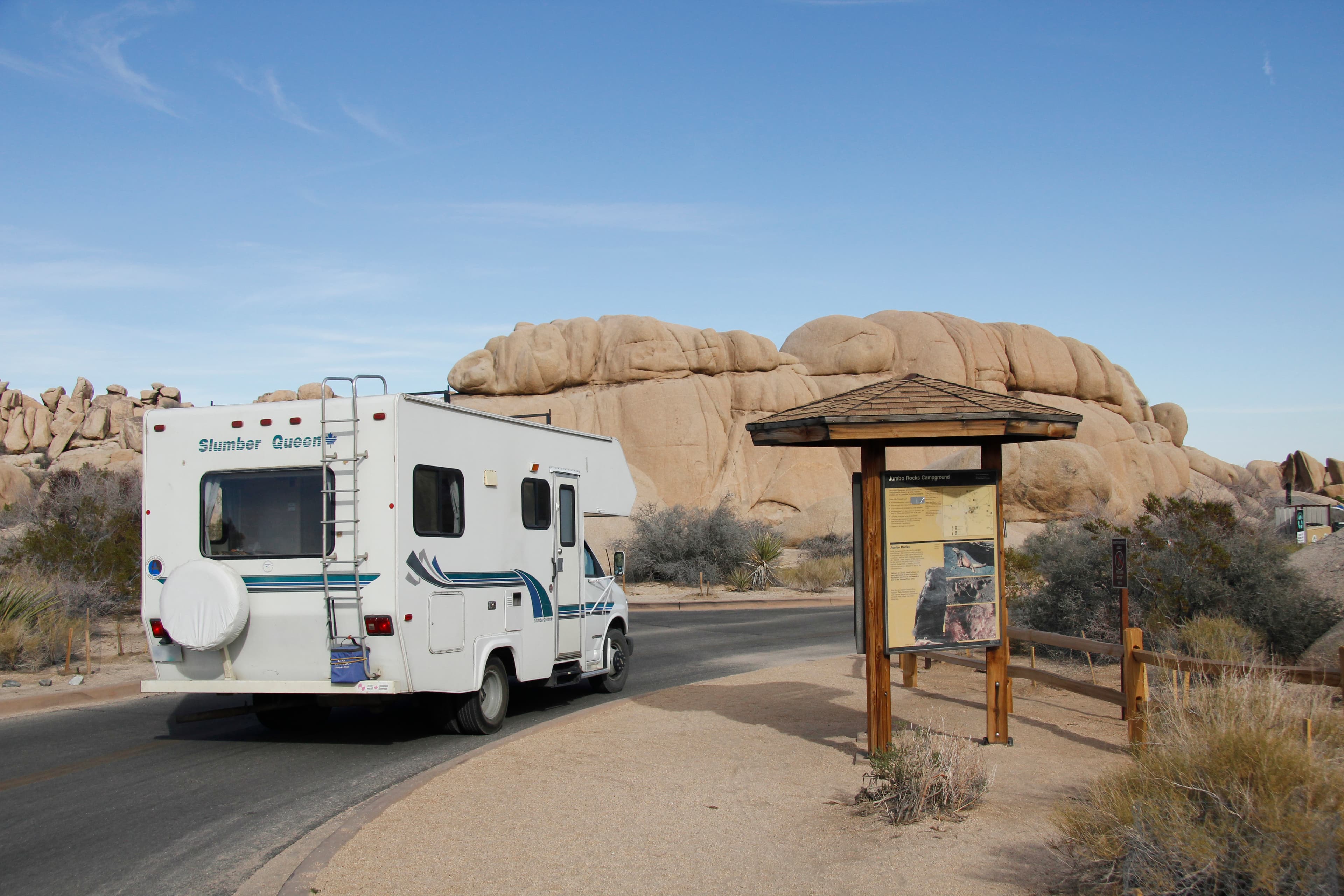 An RV drives past an campground information board.
