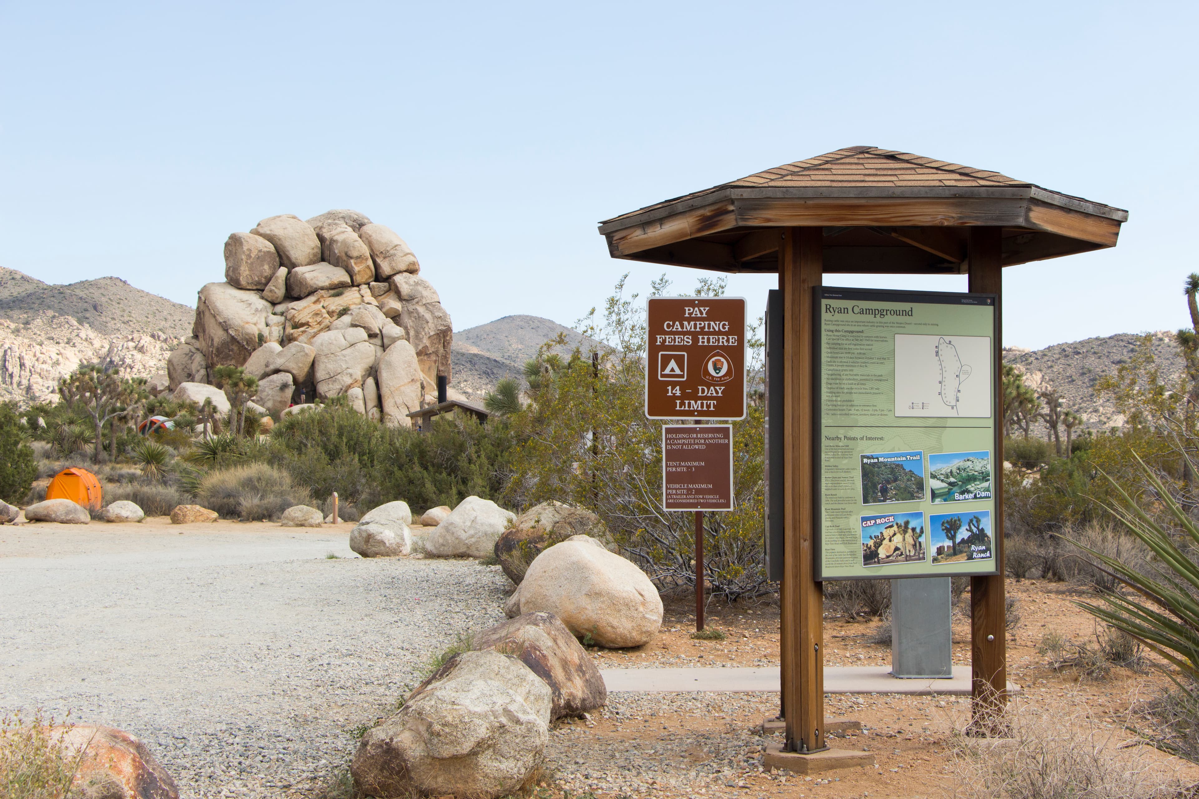 An unpaved road and campground signage is surrounded by vegetation and rock formations.