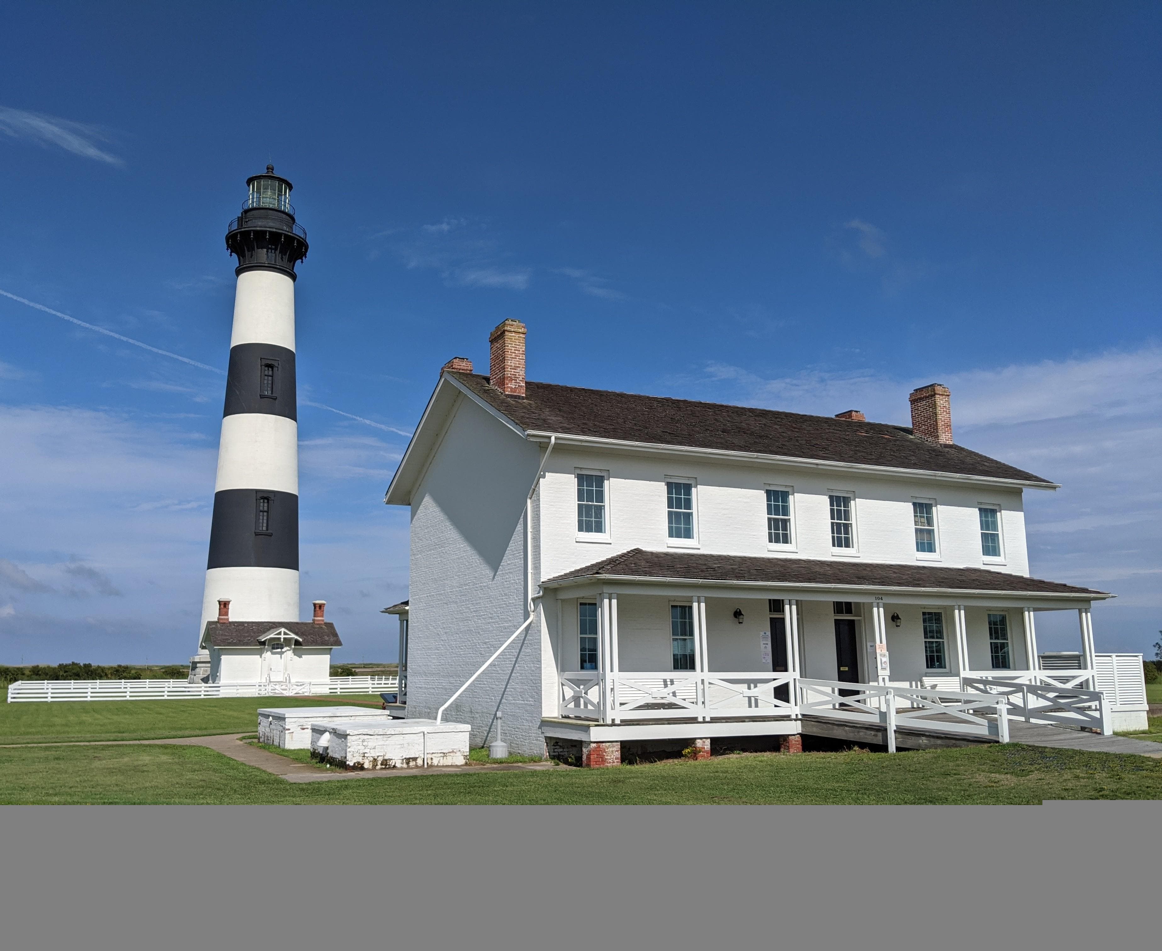 A 2 story white building in front of a black and white stripped Lightouse