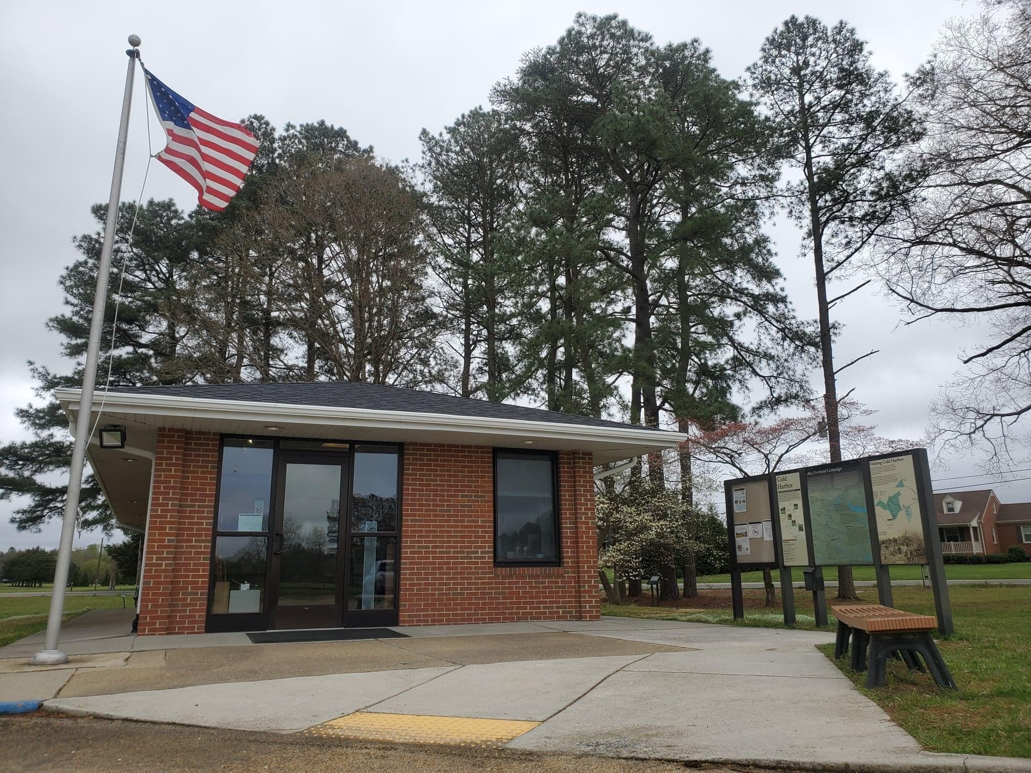 A small brick visitor center building flanked by a flagpole and a freestanding interpretive sign.