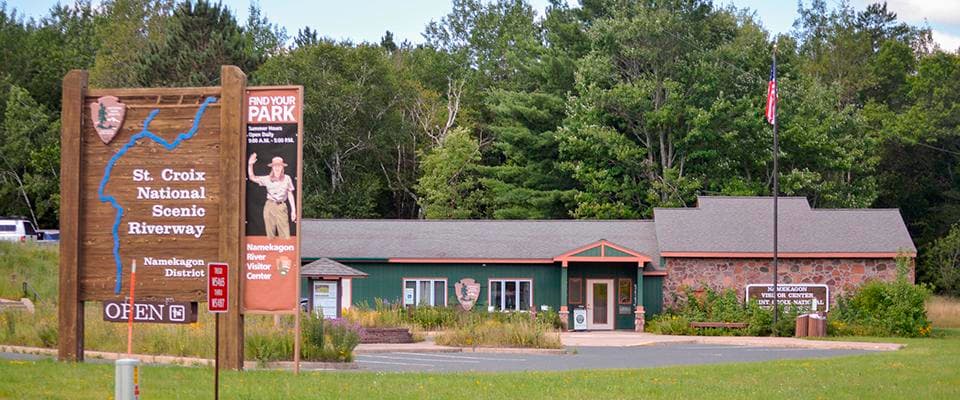 A large brown sign stands on the left with a narrow, single-story building in the background.