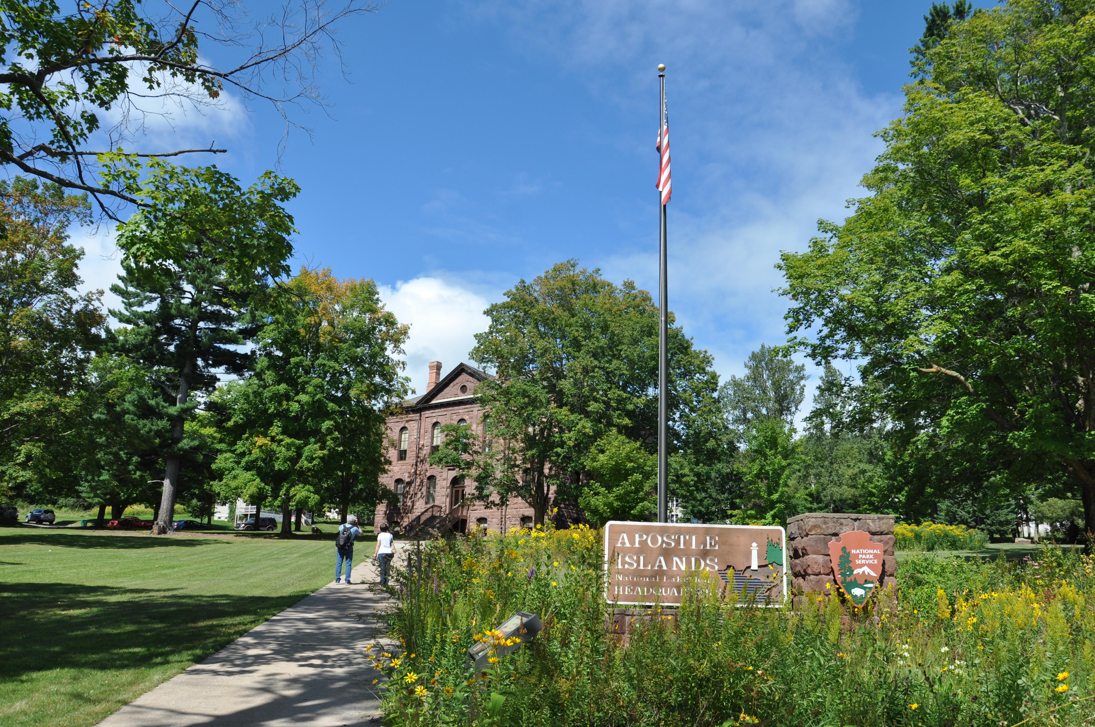A sign with an Arrowhead and flagpole in front of a large brownstone building.