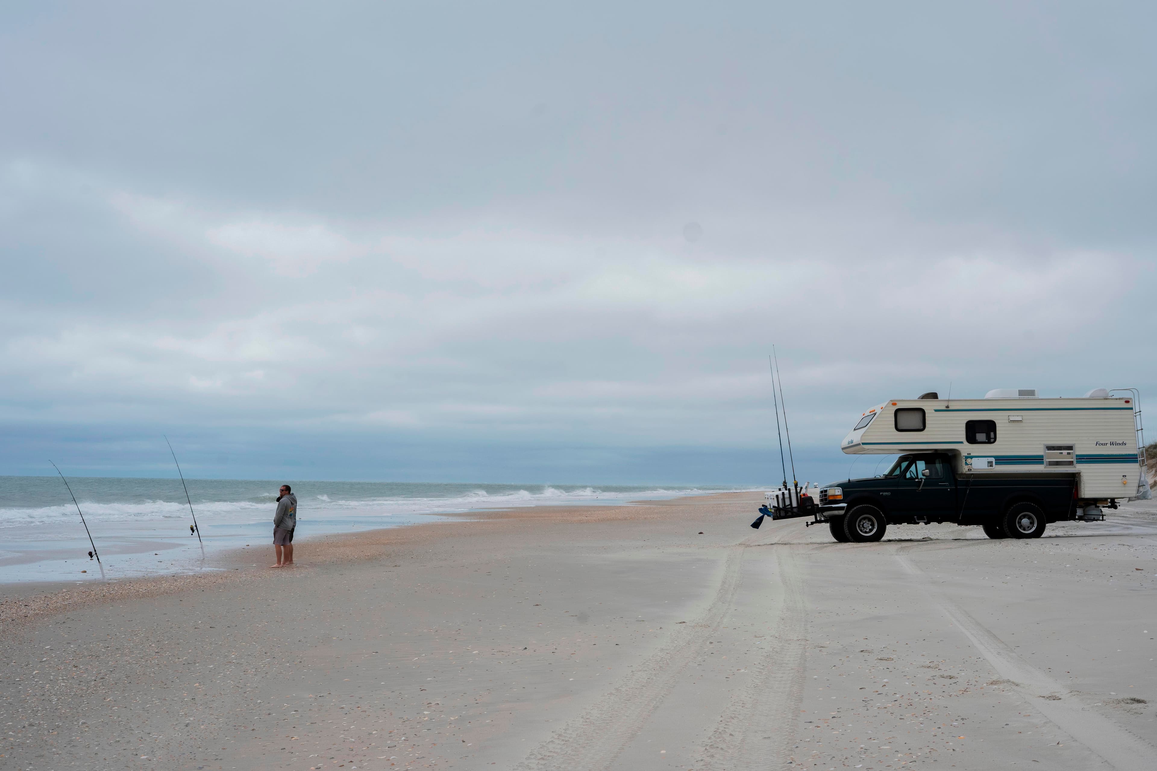 An angler stands at the shore with his vehicle behind him.