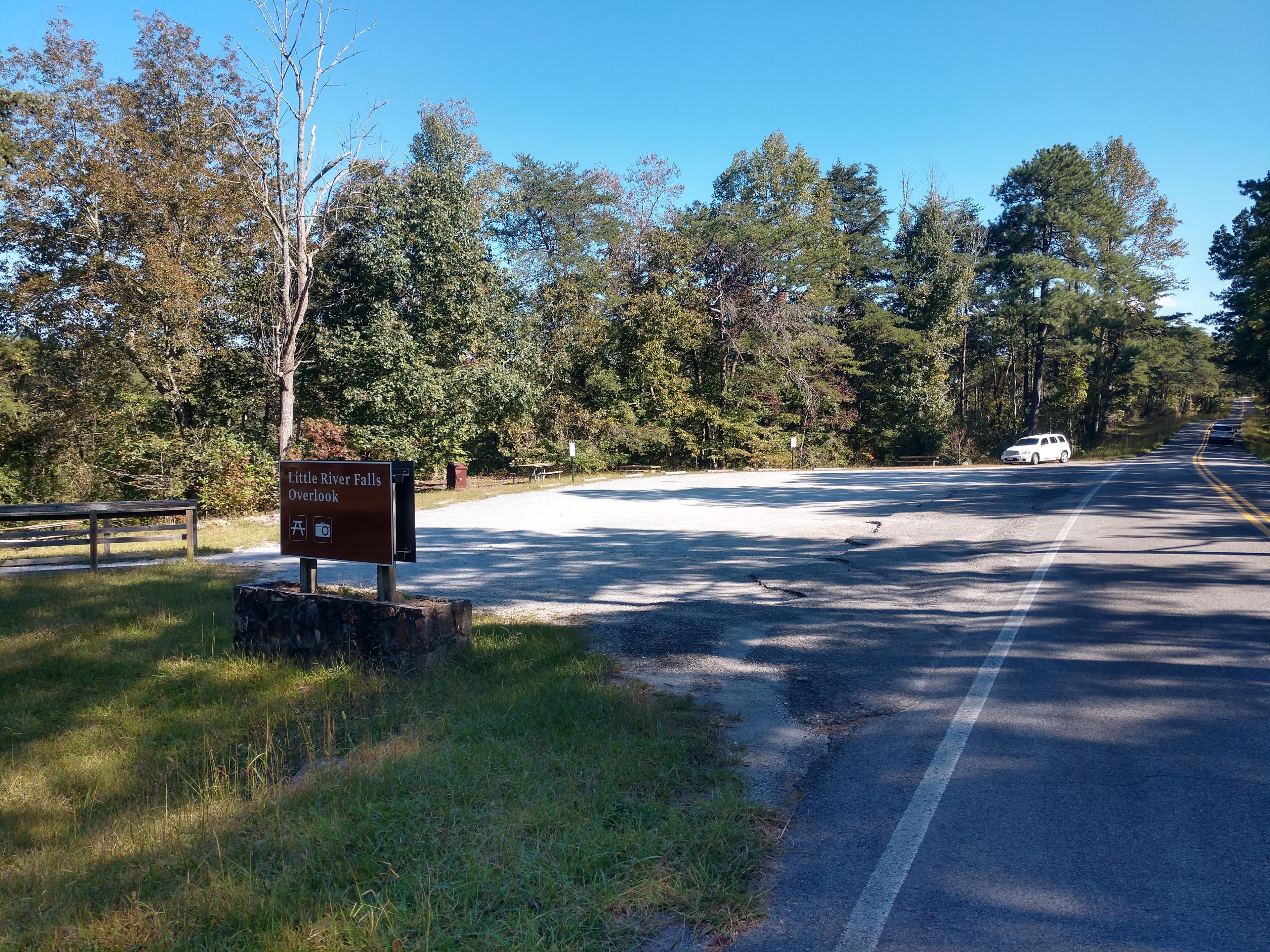 A small roadside gravel parking area with a mixed conifer and deciduous forest around it.