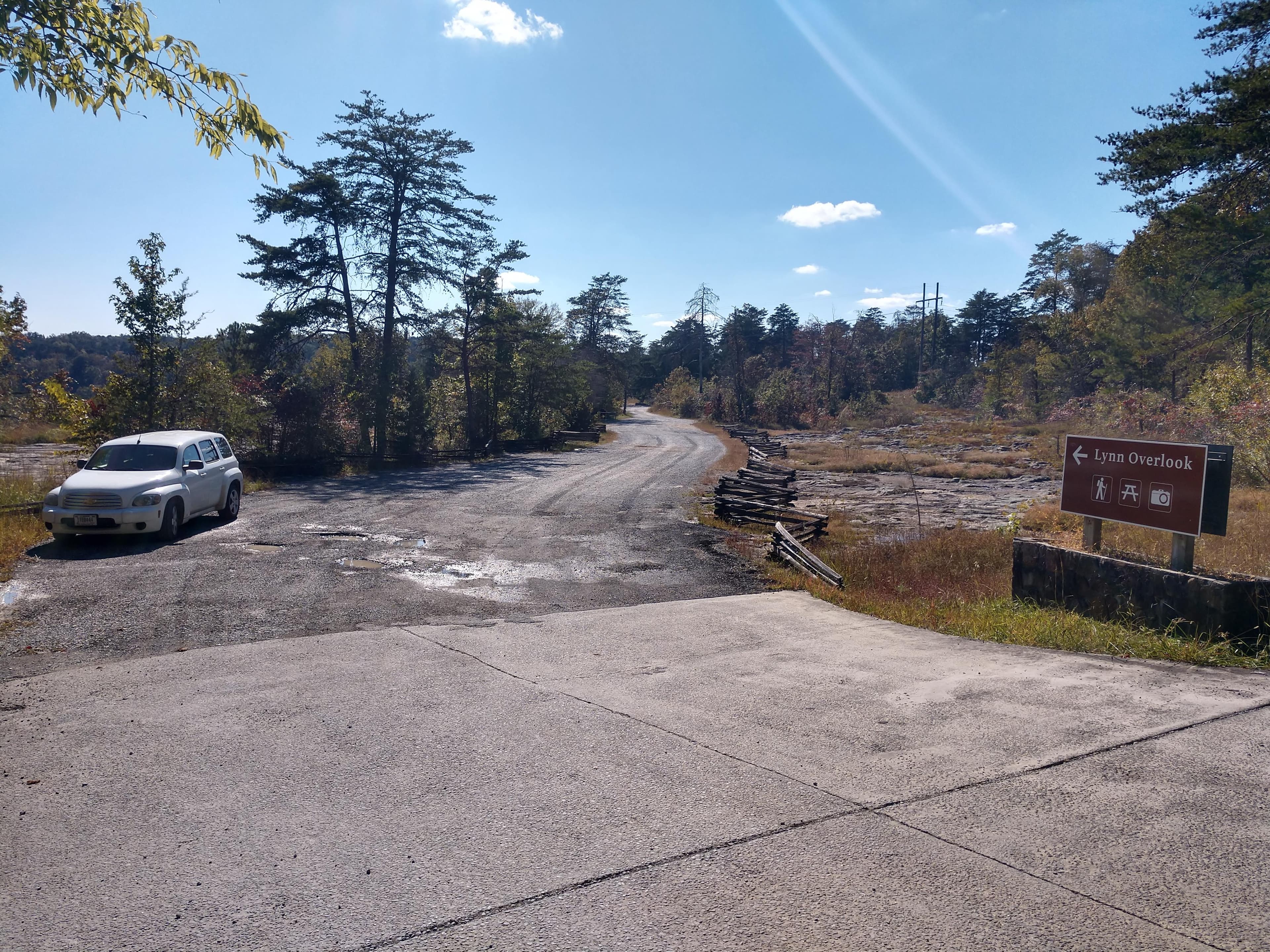 A small roadside gravel parking area with a mixed conifer and deciduous forest around it.