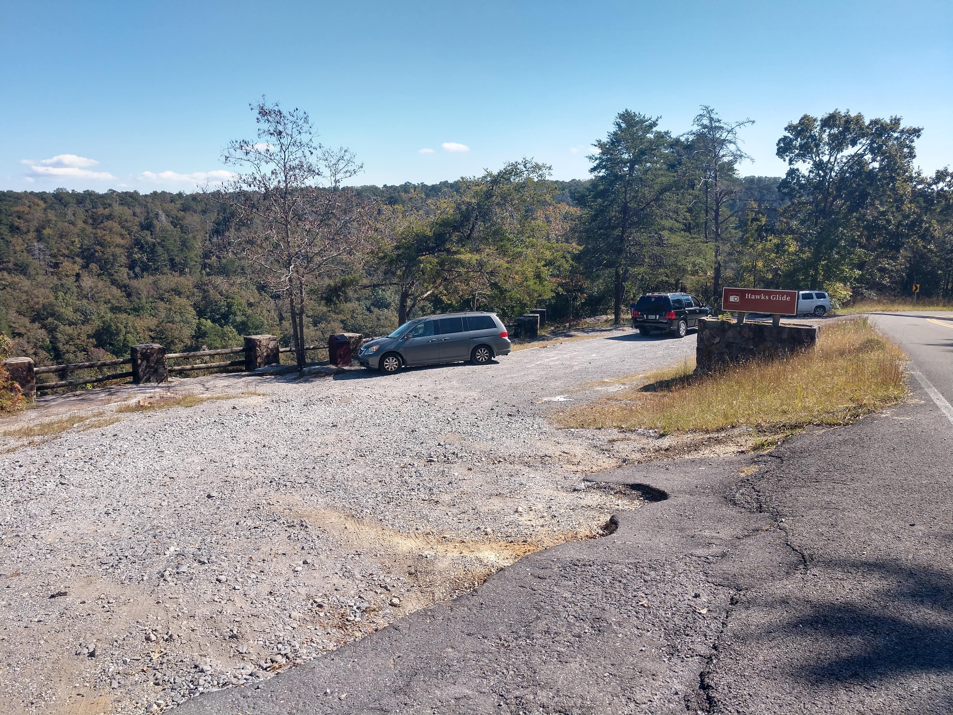 A small roadside gravel parking area with a mixed conifer and deciduous forest around it.
