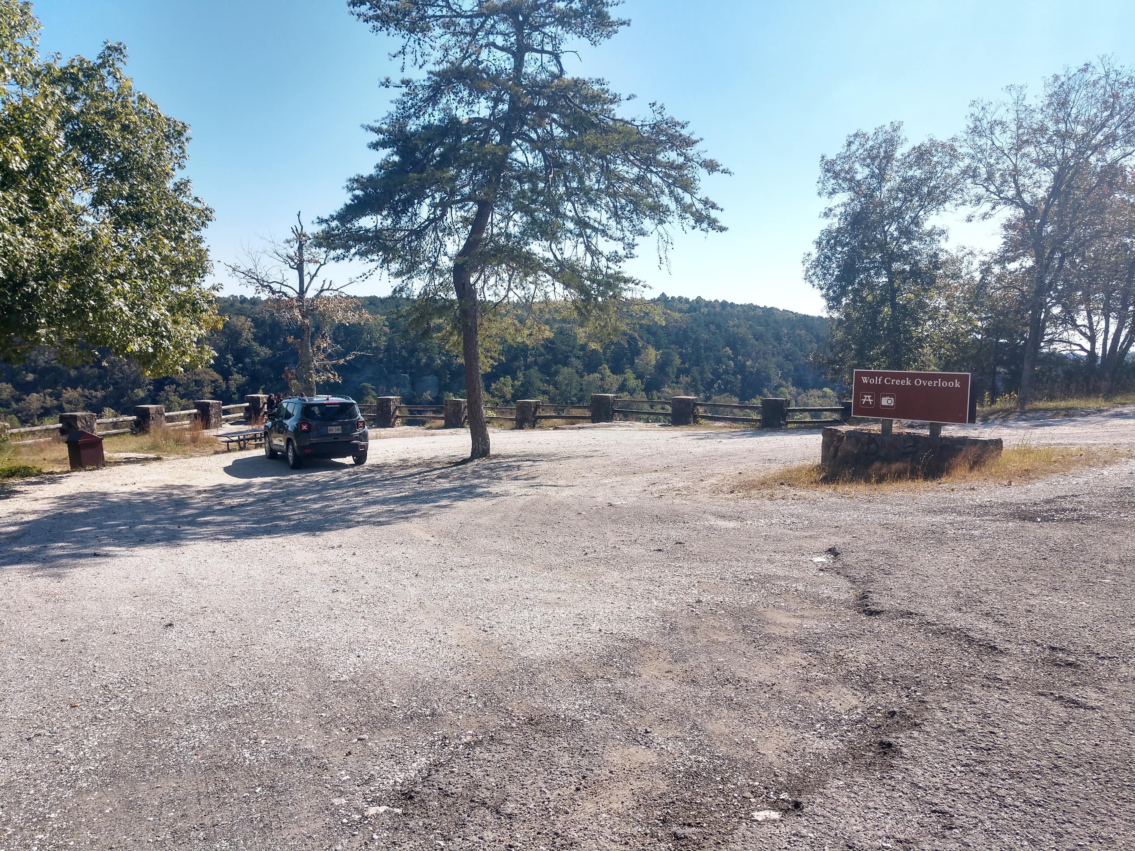 A small roadside gravel parking area with a mixed conifer and deciduous forest around it.