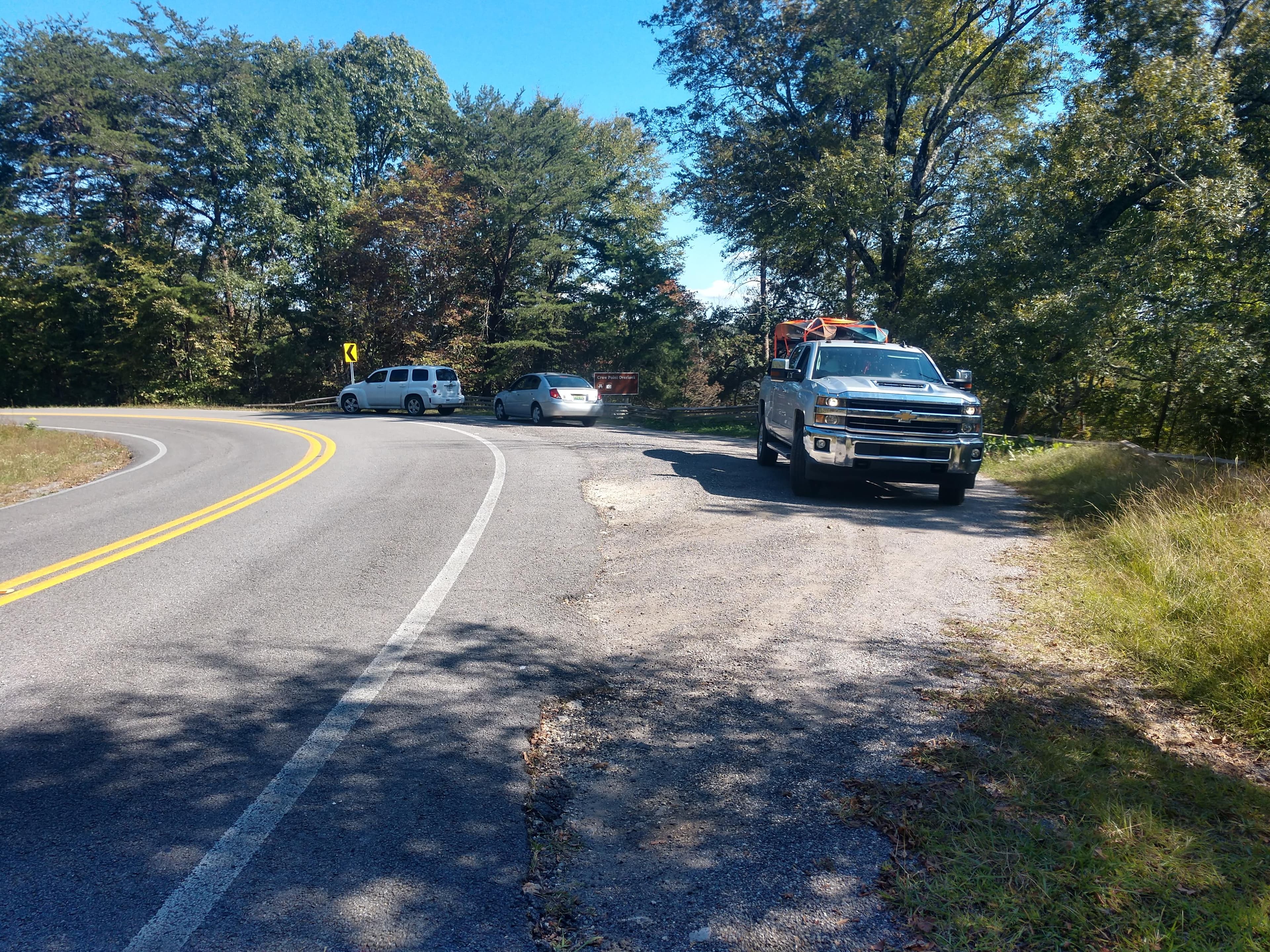 A small roadside gravel parking area with a mixed conifer and deciduous forest around it.