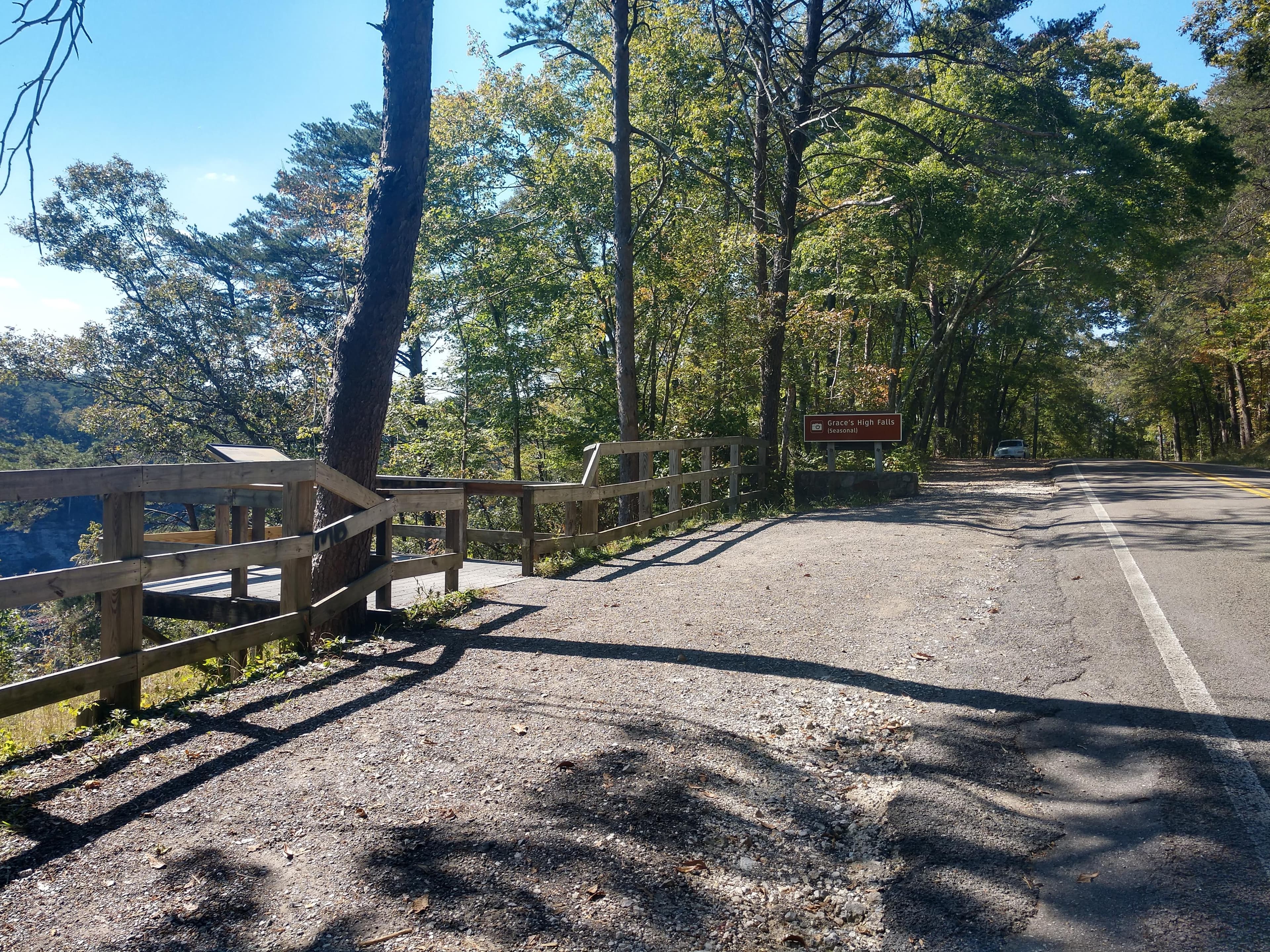 A small roadside gravel parking area with a mixed conifer and deciduous forest around it.