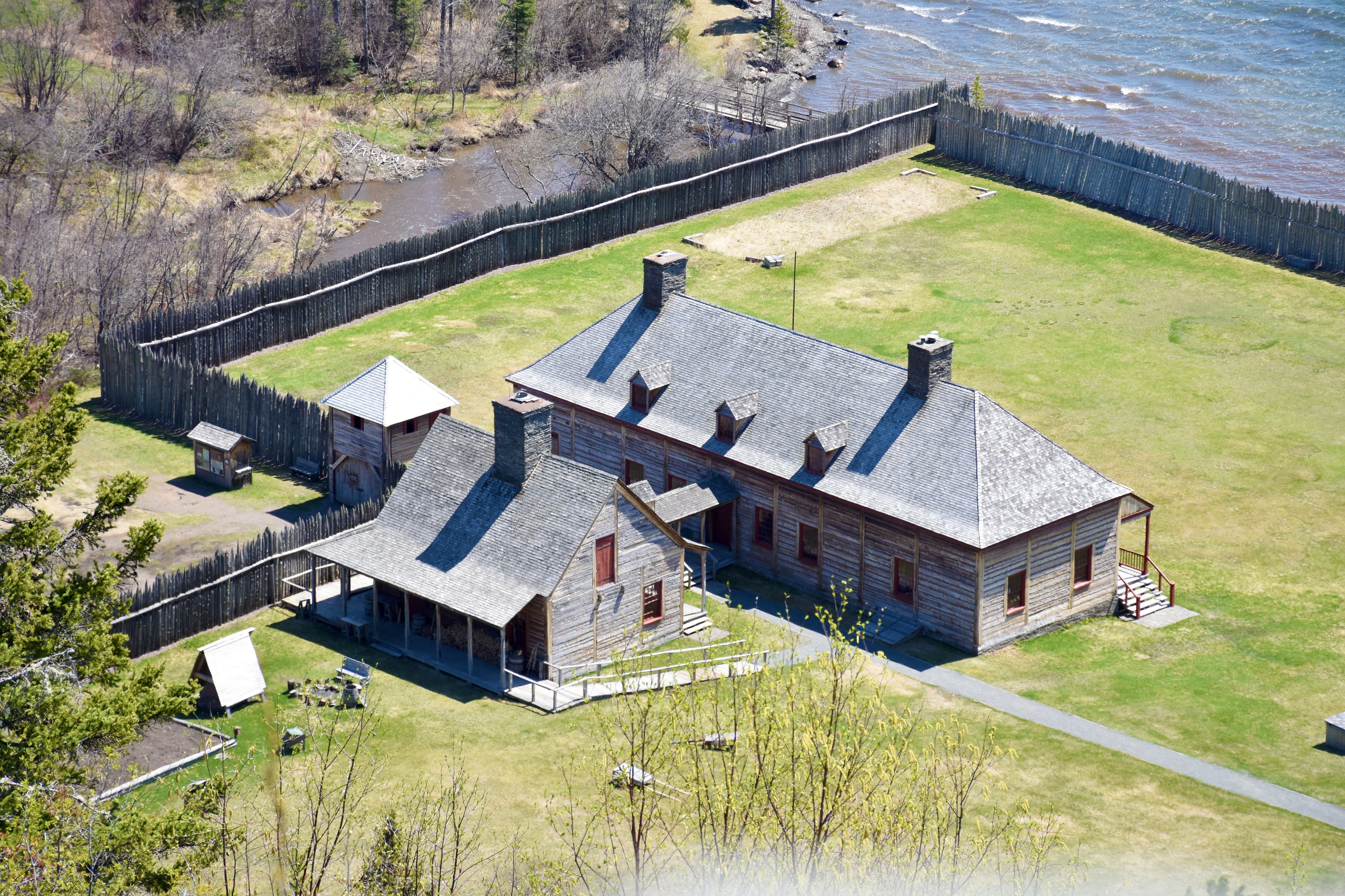 Historic buildings within a stockade, adjacent to a creek that empties into a lake.