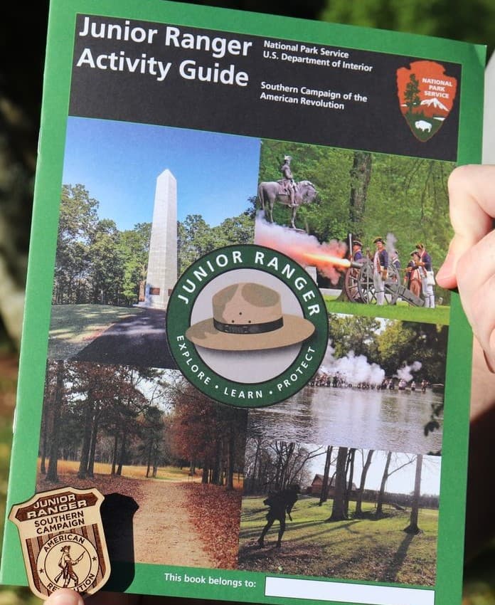 The cover of a junior ranger booklet with the wooden badge held in the lower left corner.