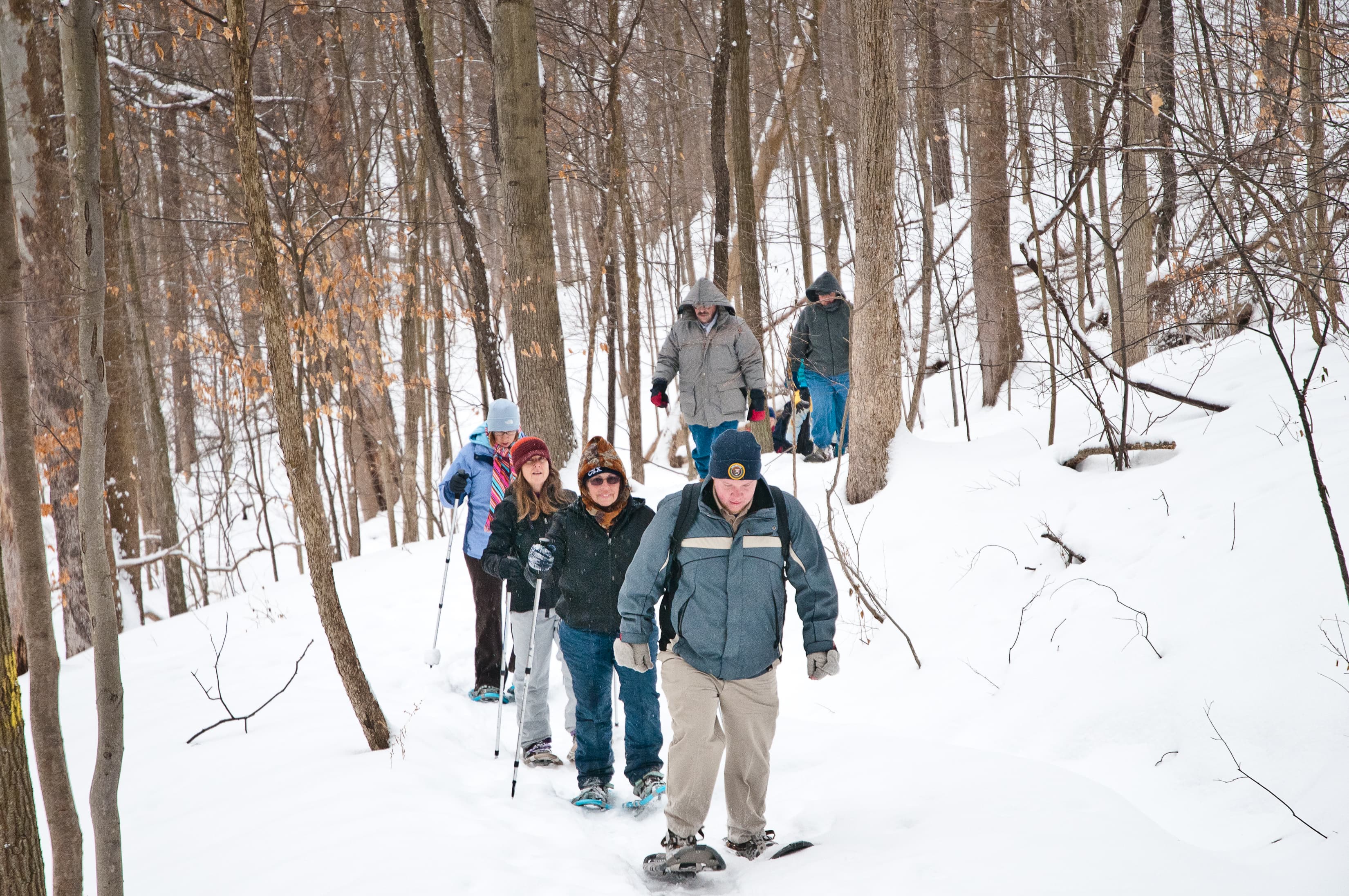 A group of people in winter hats snowshoes along a snow-covered trail in the forest.