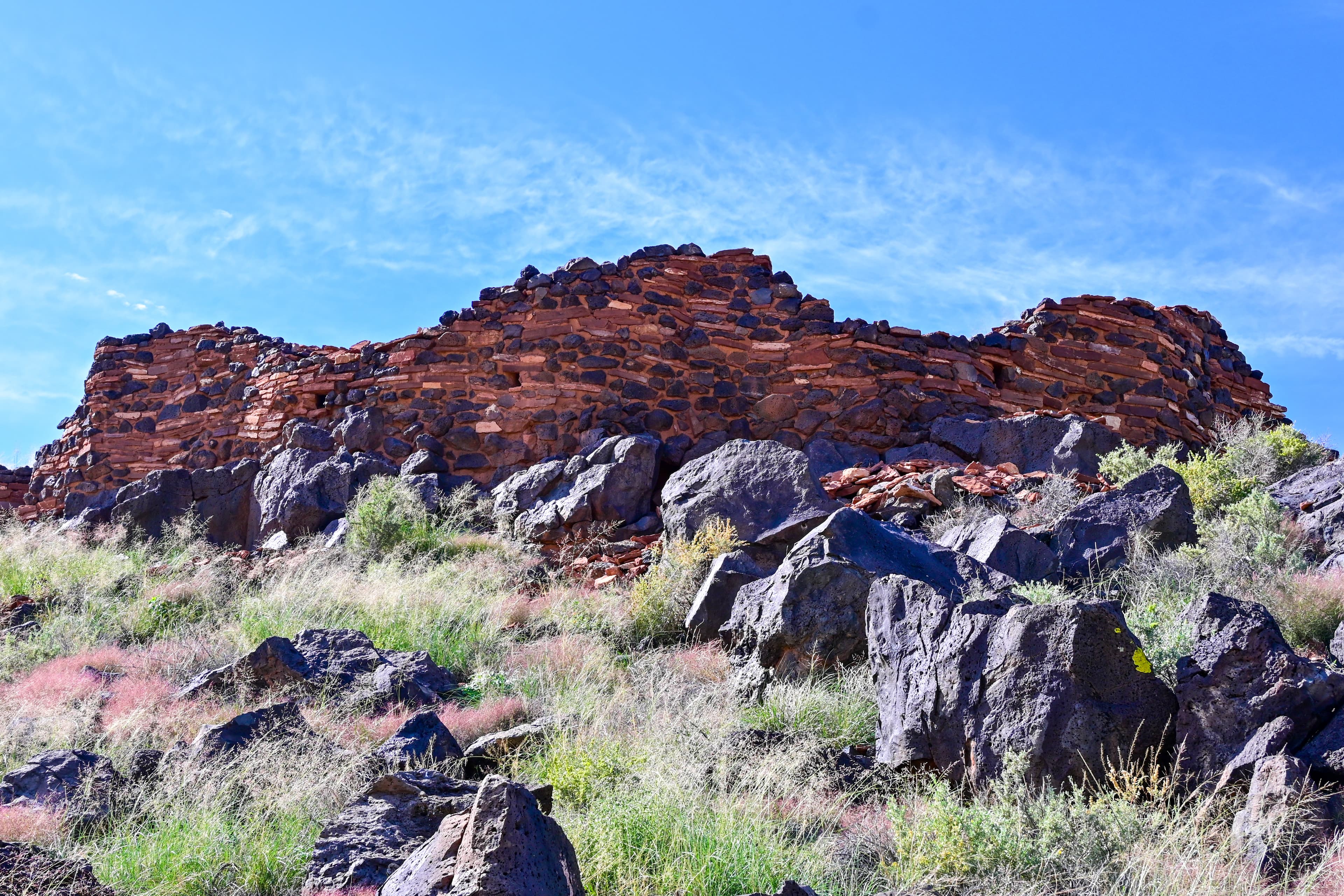 A red sandstone and black basalt pueblo sits atop a hill.