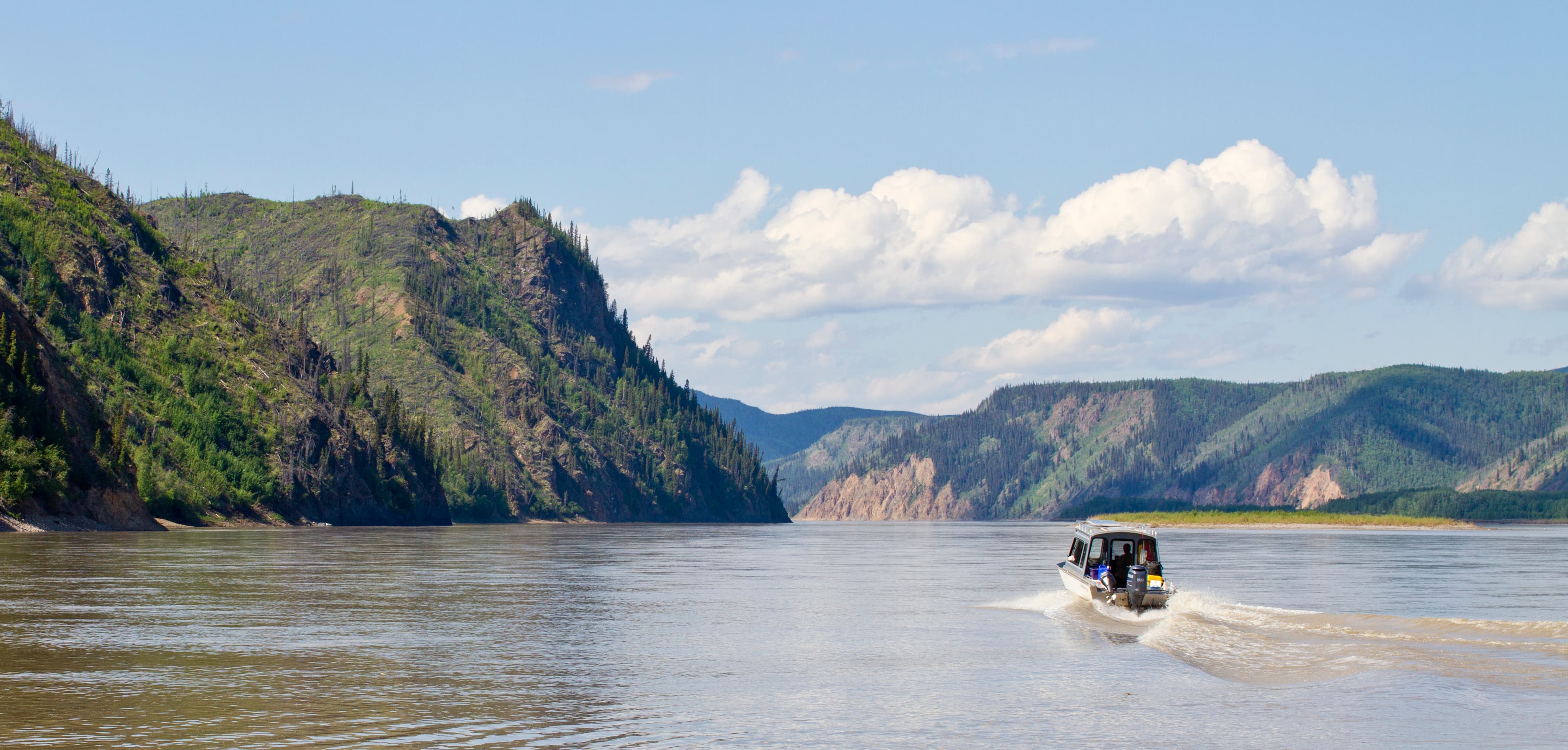 Boat traveling down the Yukon River with bluffs on each side