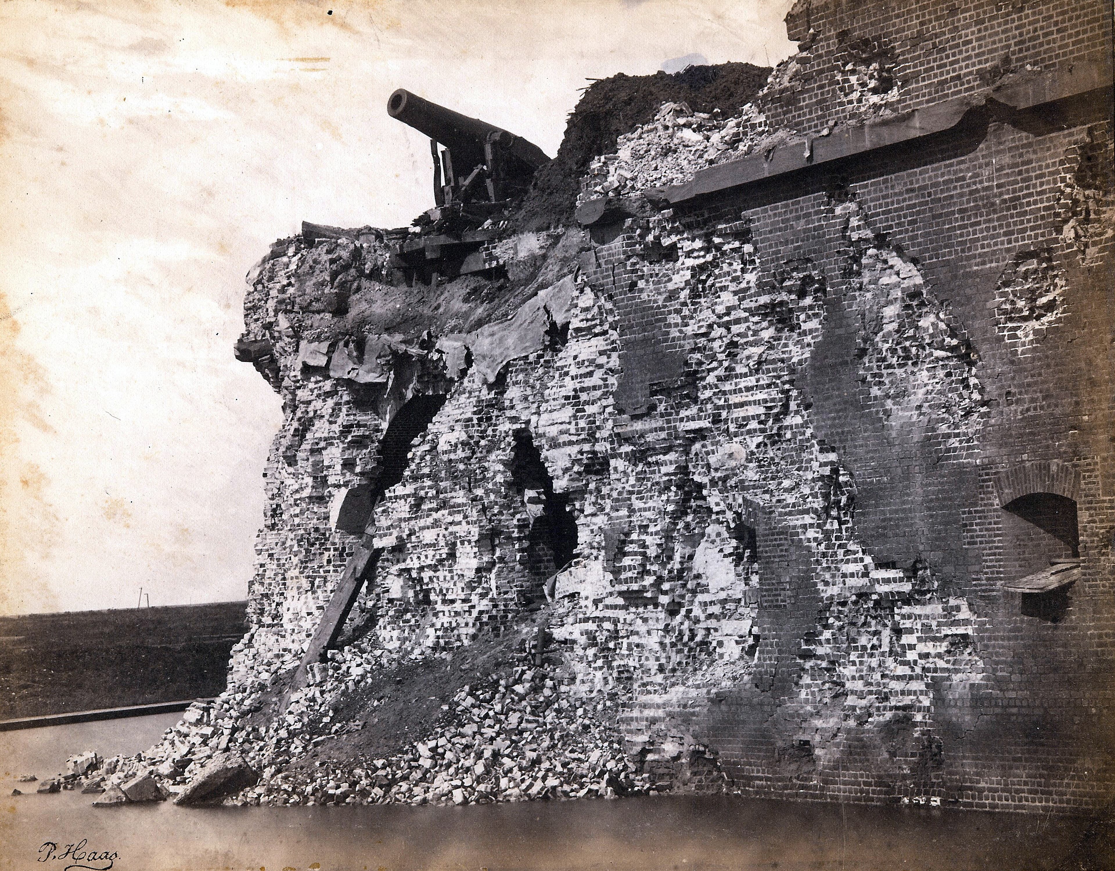 A destroyed brick wall with a cannon on top hanging over the edge.