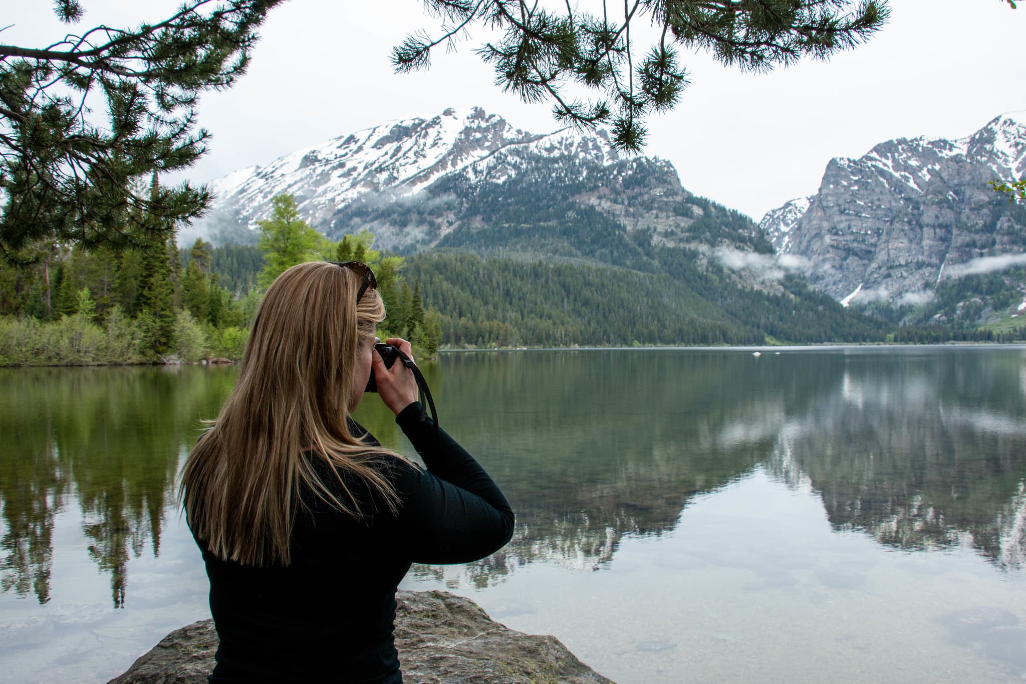 A woman takes a picture beside a lake.