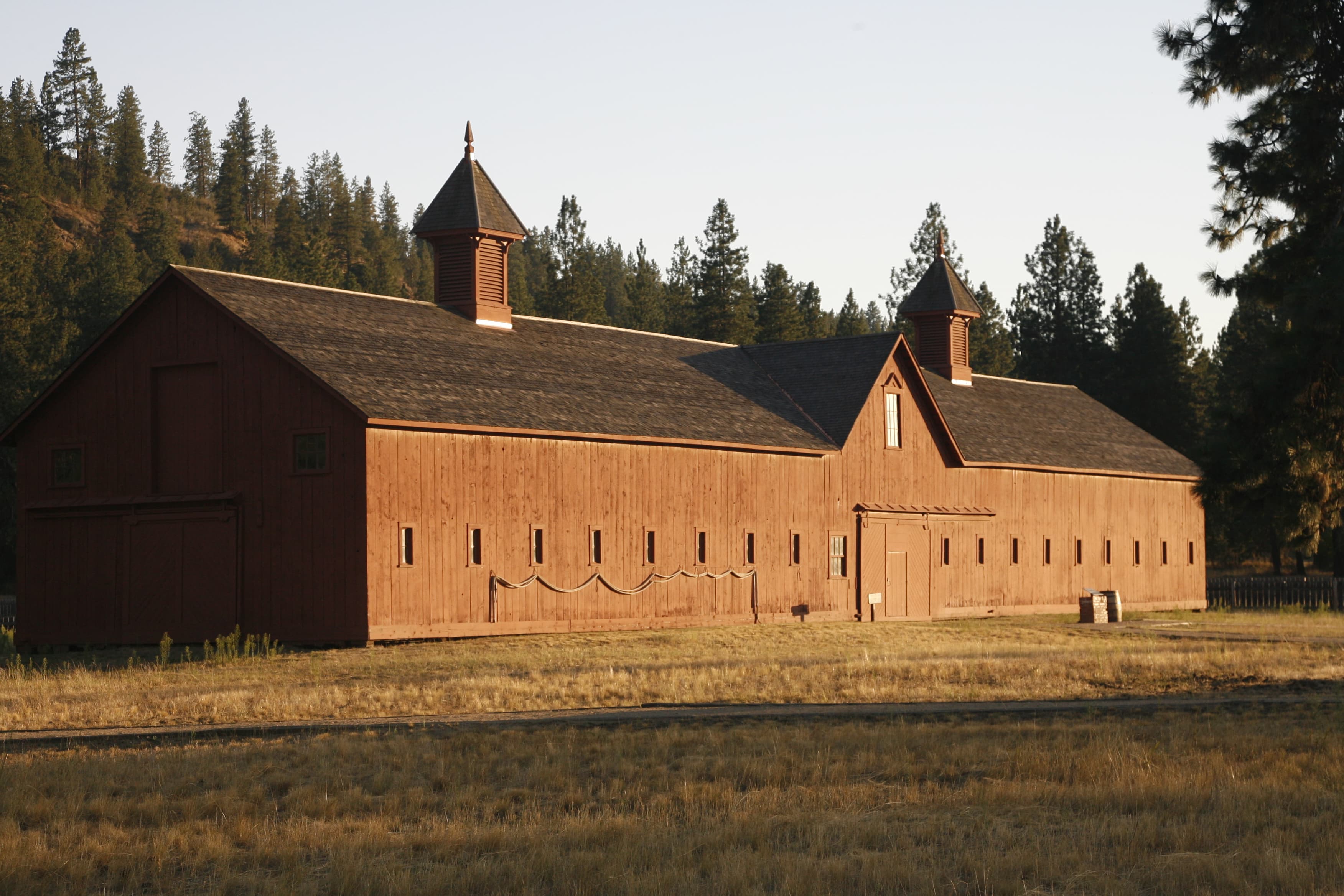 Long wood building with brown shingles and two small towers sits in a dry grassy field.