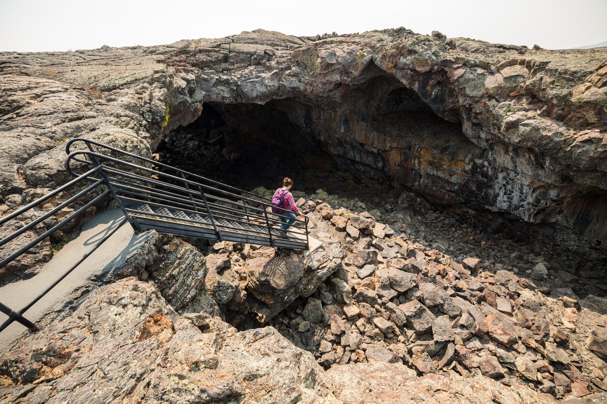 A person walks down a set out stairs into the wide open entrance of a lava tube.