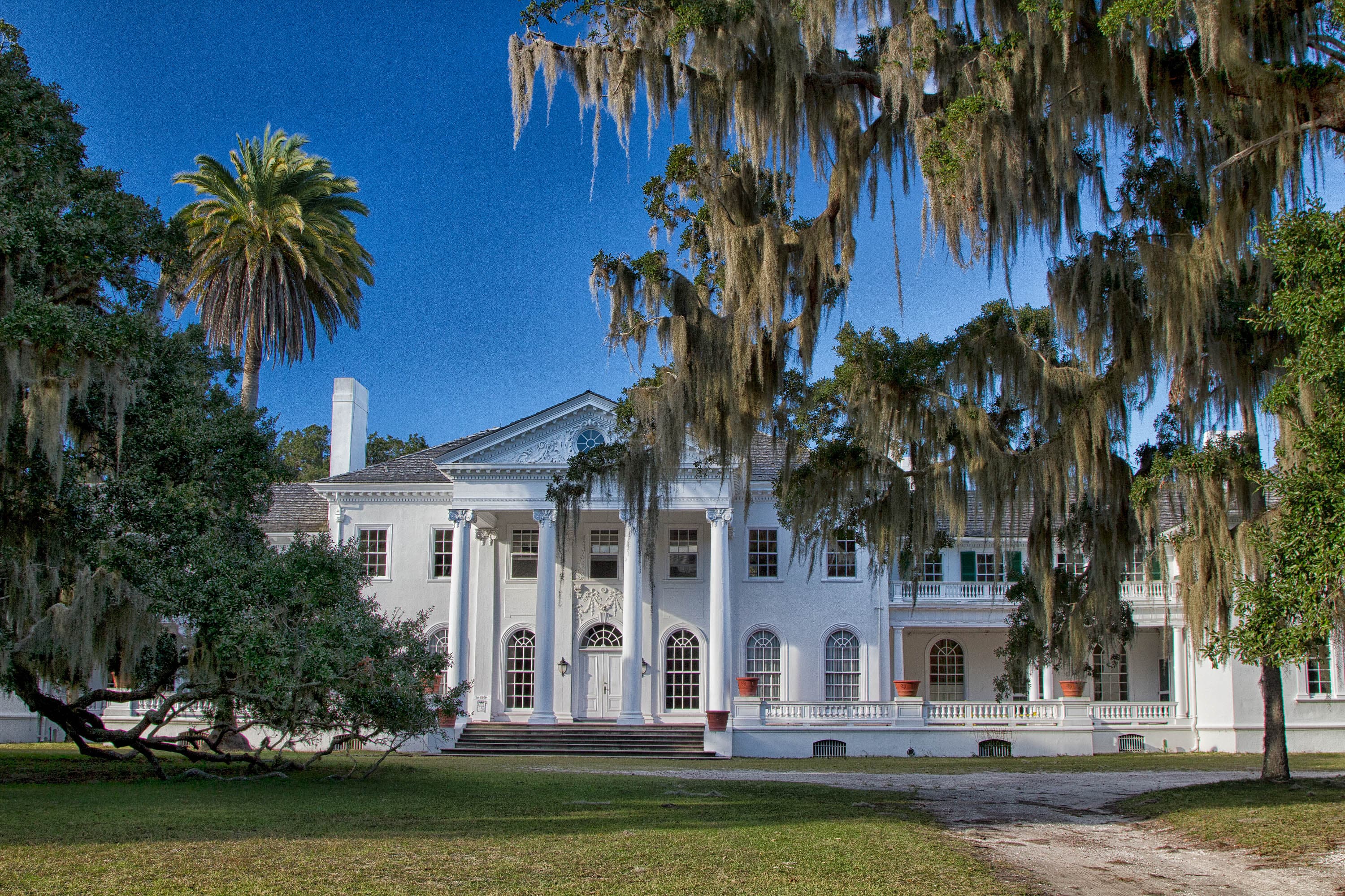 Large historic mansion and live oak trees with Spanish moss hanging down.