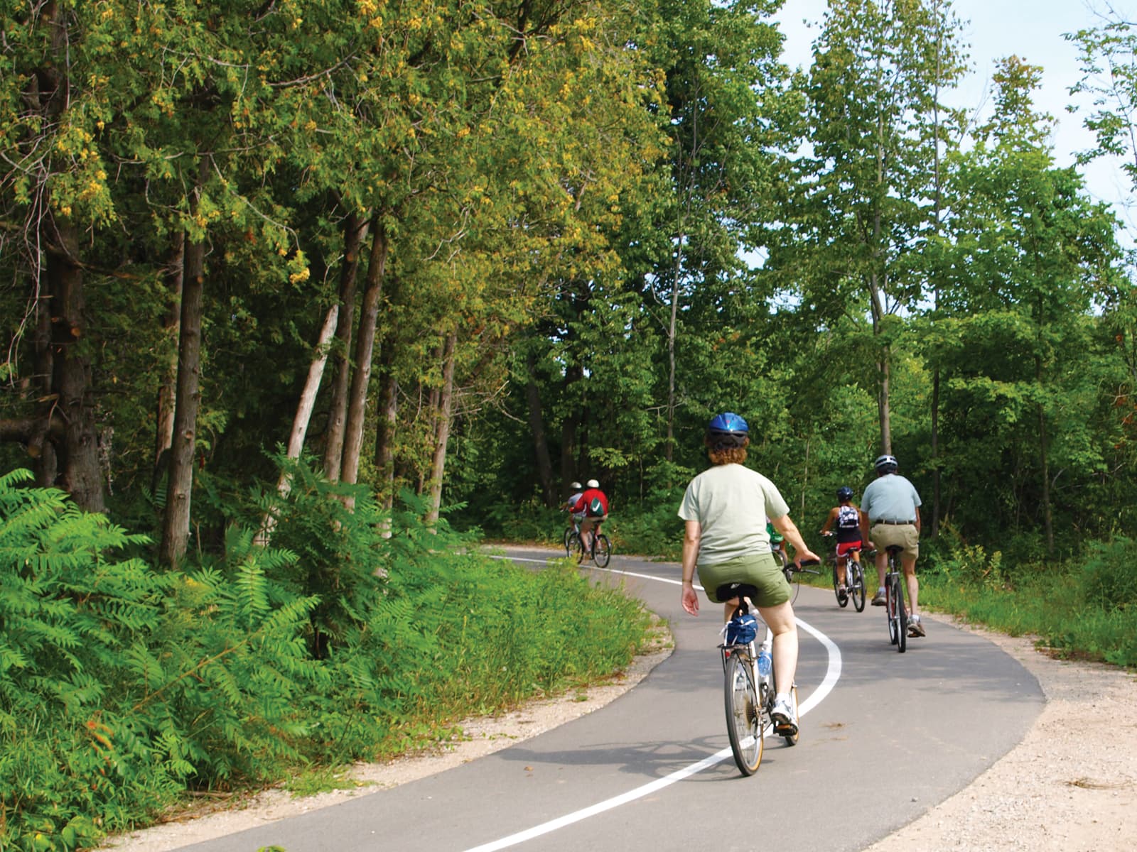 Bikers on a paved trail curving left into wooded area