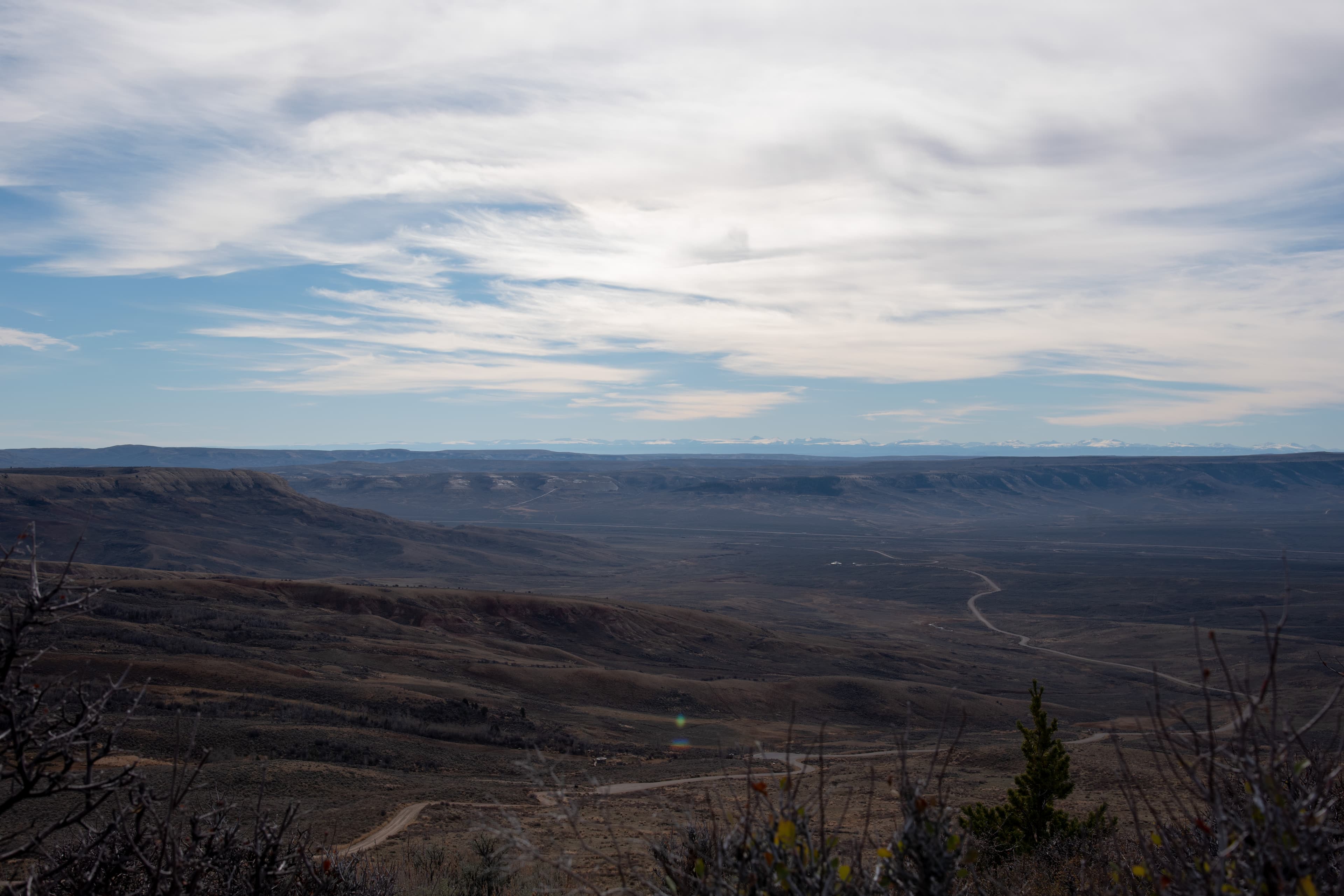 A road travels away through the valley with ridges and snow-capped mountains in the distance