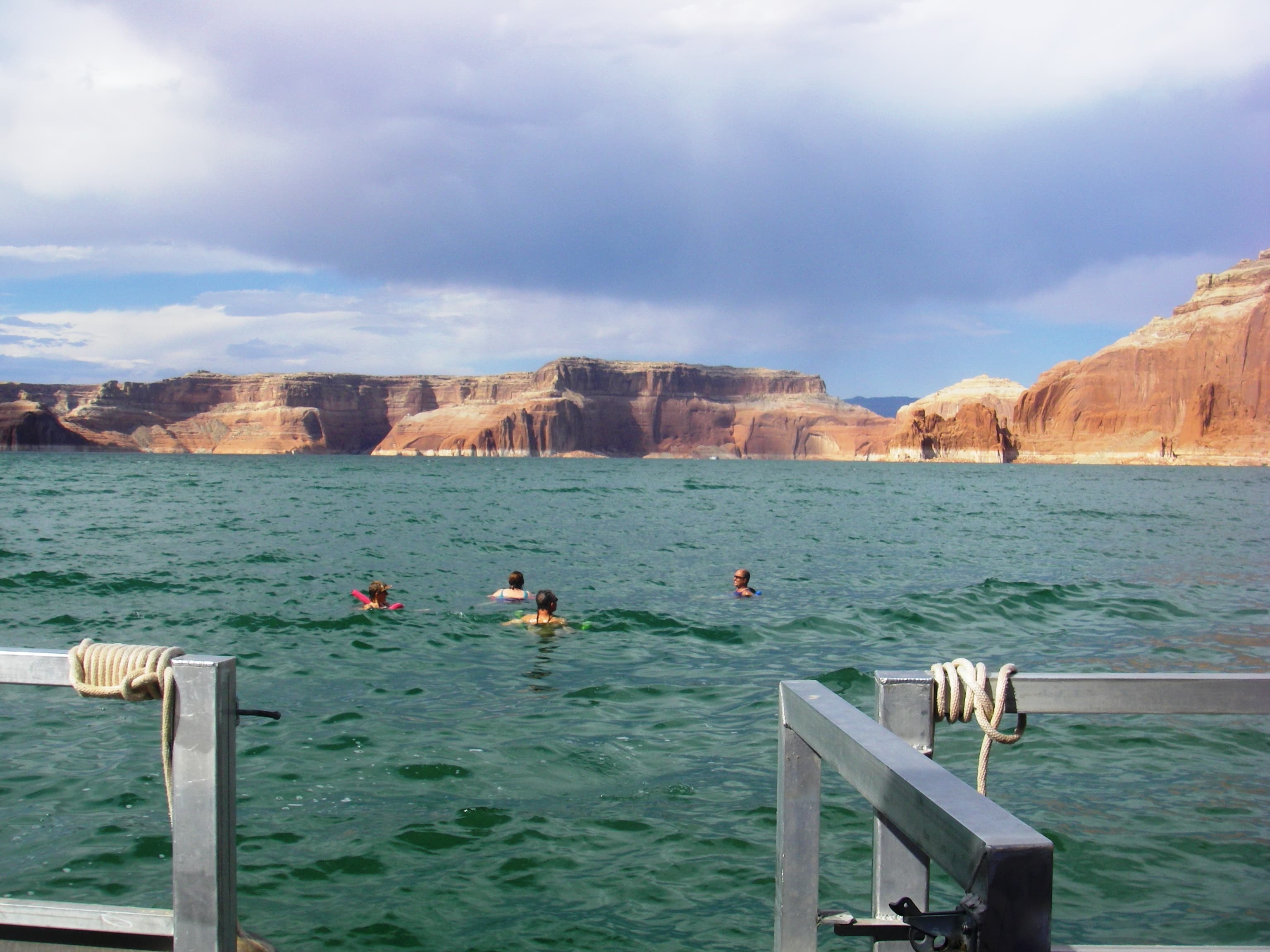 Four people swim backwards away from a houseboat railing