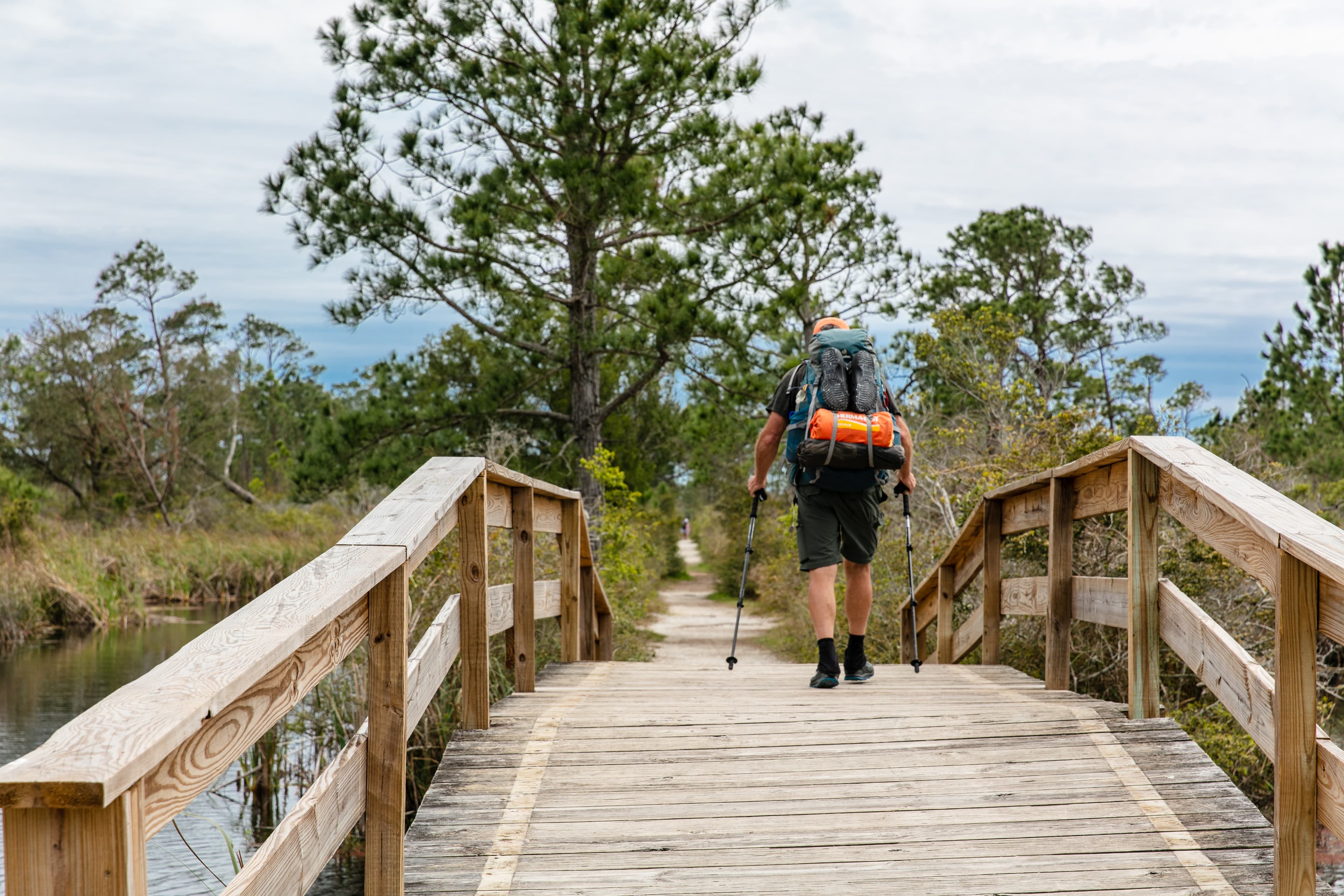 A backpacker crosses over a bridge with poles in hand.