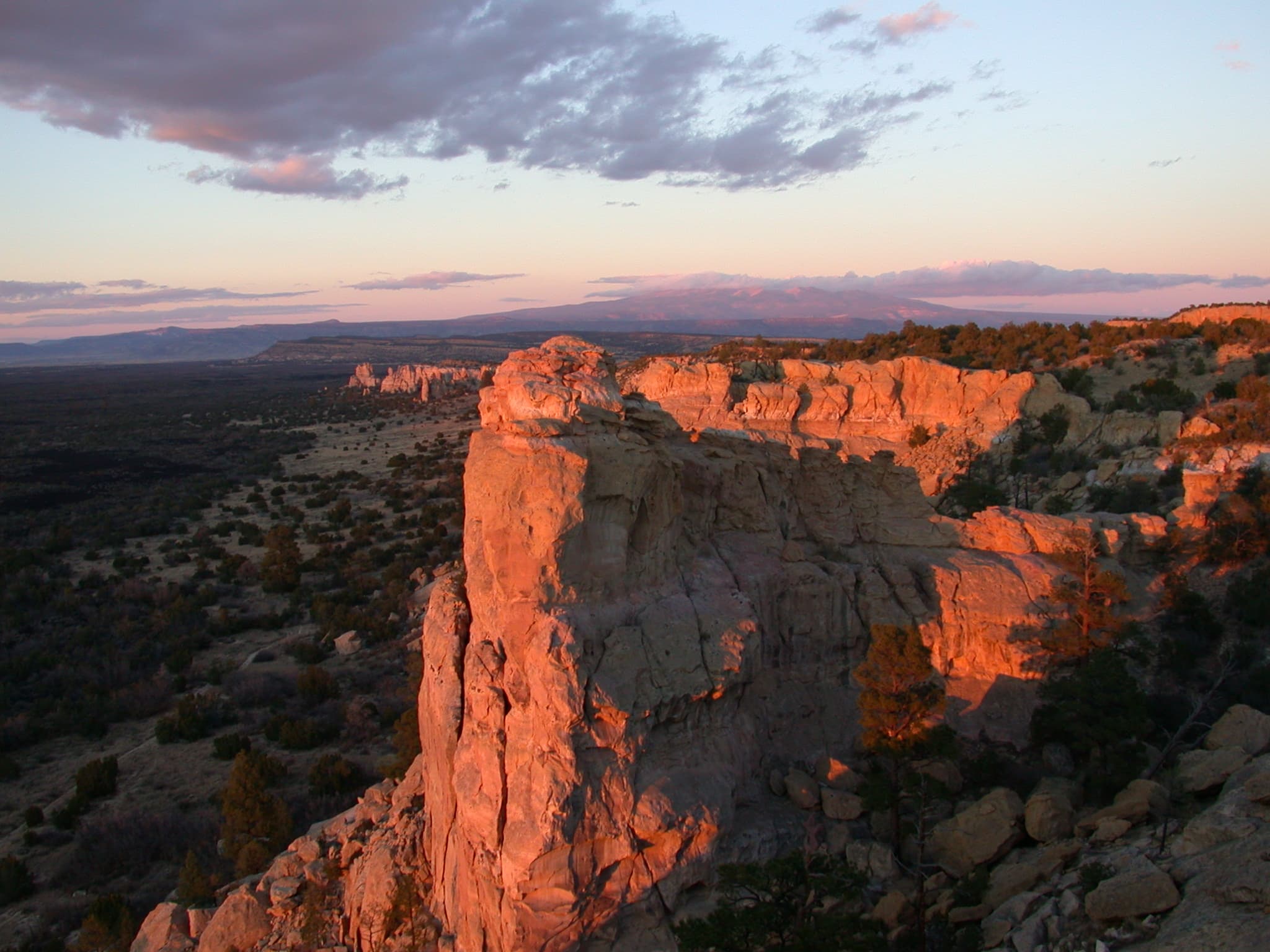 a tall sandstone bluff colored red by sunset under a darkening sky