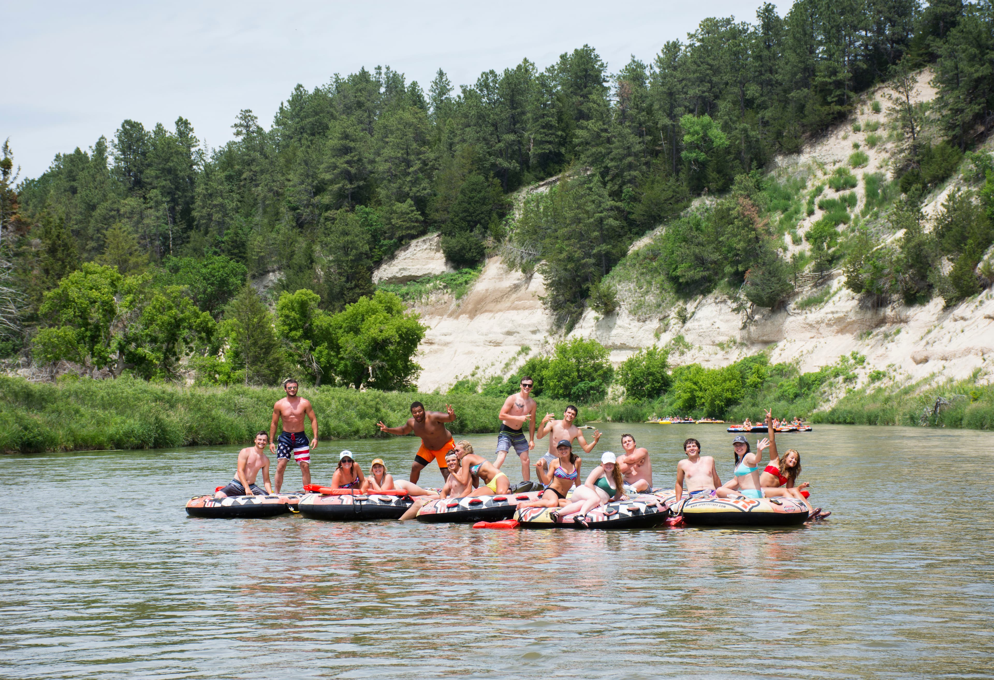 a collection of 7 tubes on the river, with 13 people floating on them; they are tied together.