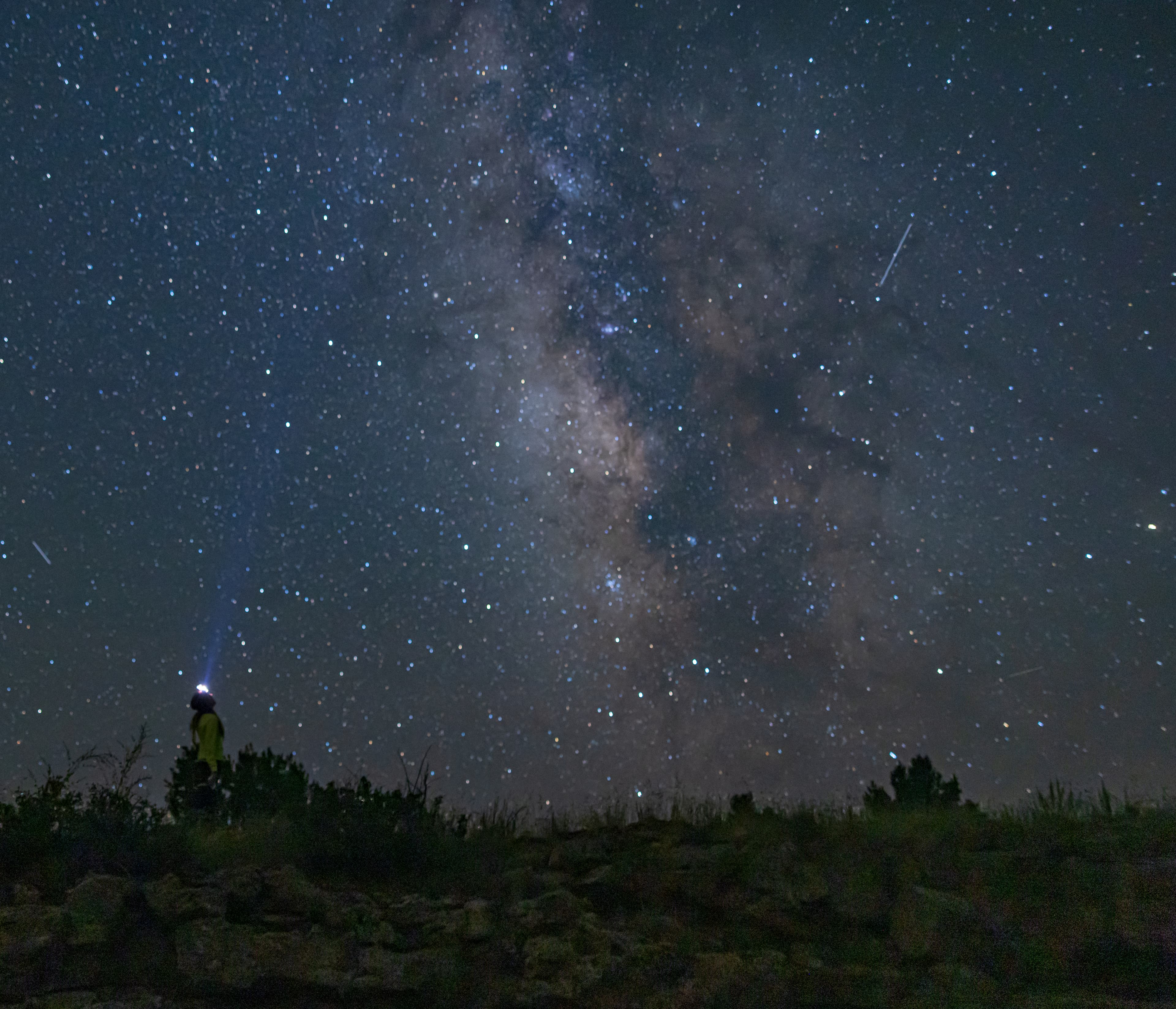A hiker with a headlamp looks up at the star-filled night sky. The Milky Way Galaxy creates a band o