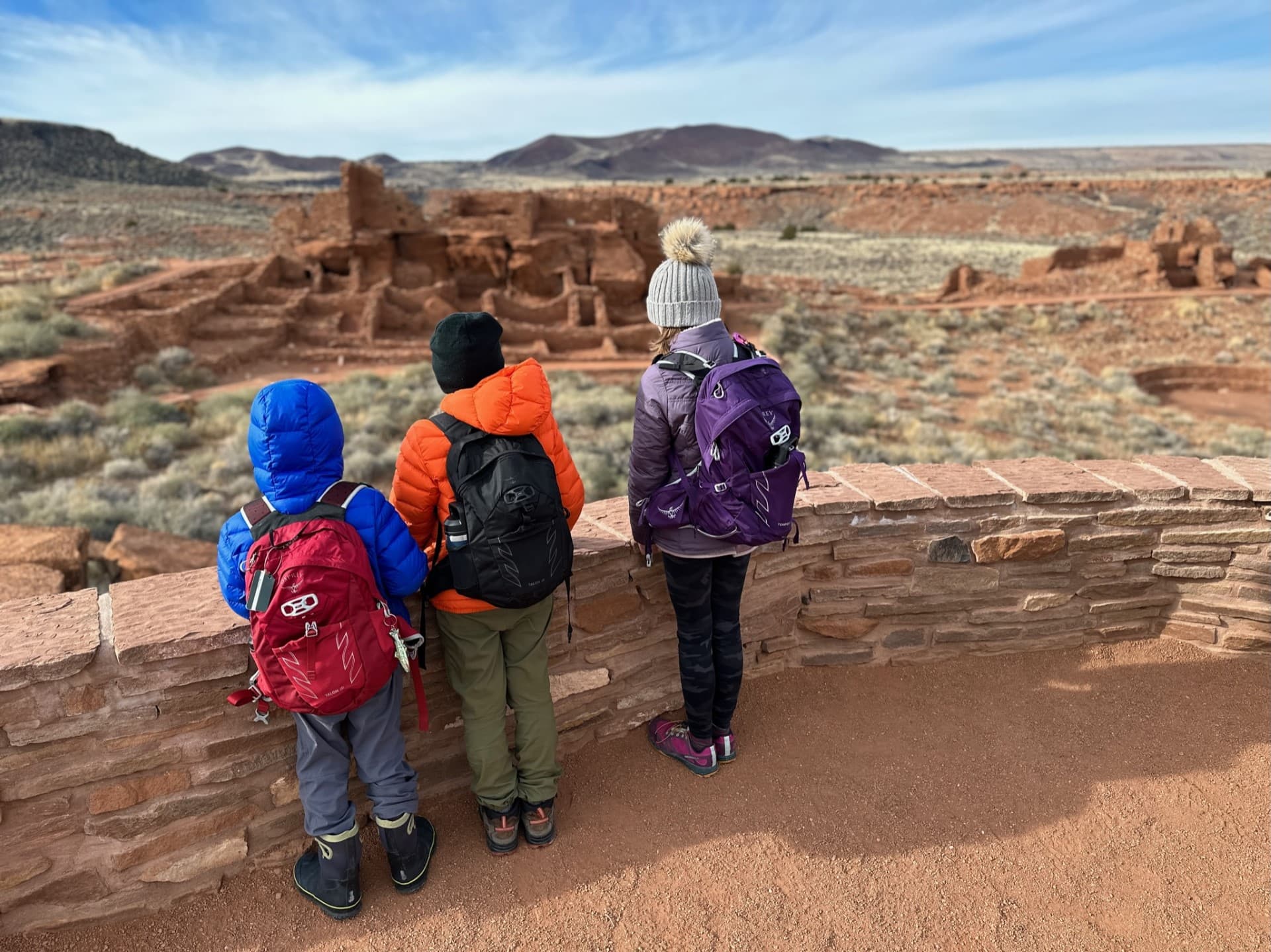 Three Jr. Rangers standing at the Wupatki trail overlook viewing Wupatki Pueblo.