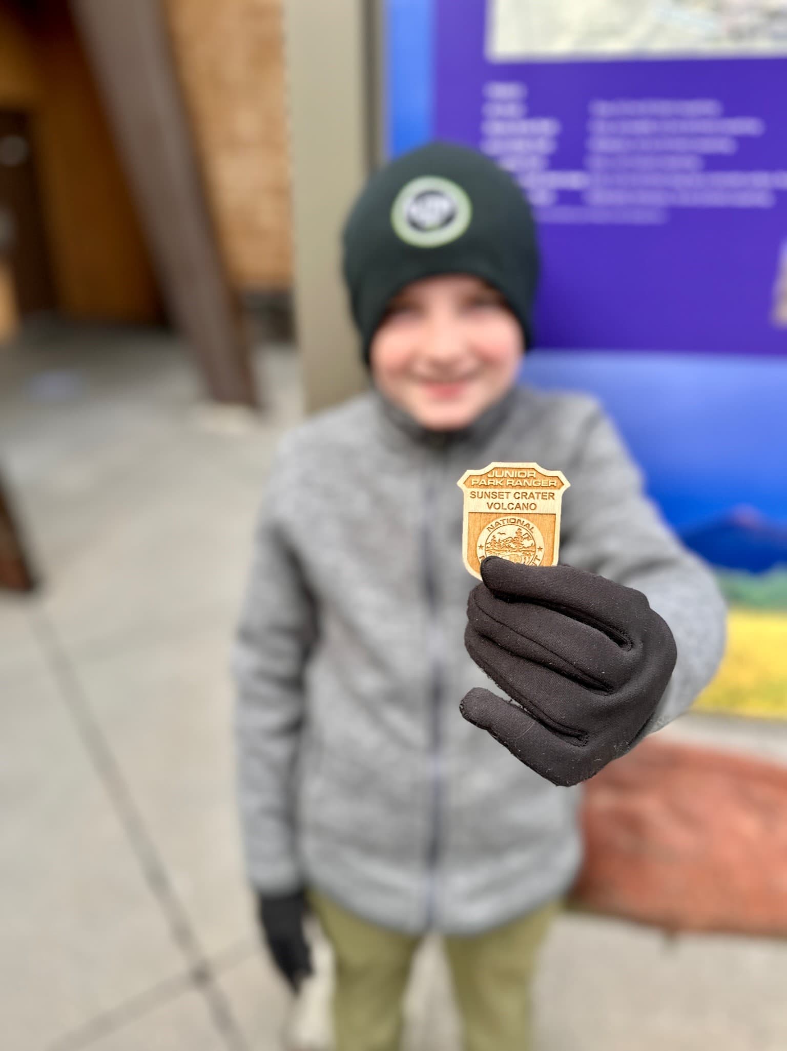 A child wearing cold weather clothing holds up their Jr. Ranger badge.