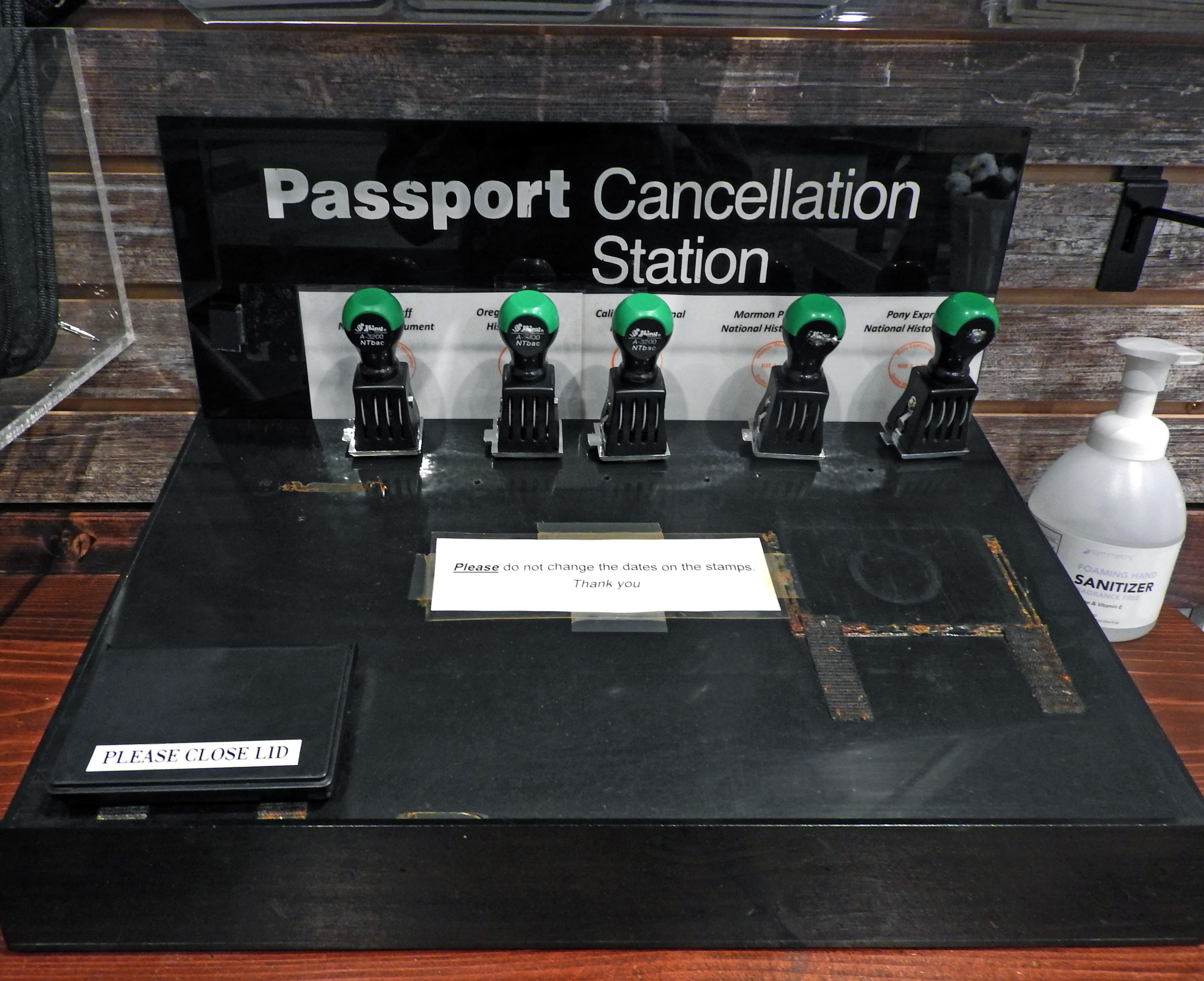 Five rubber stampers rest on a black shelf labeled "Passport Cancellation Station."