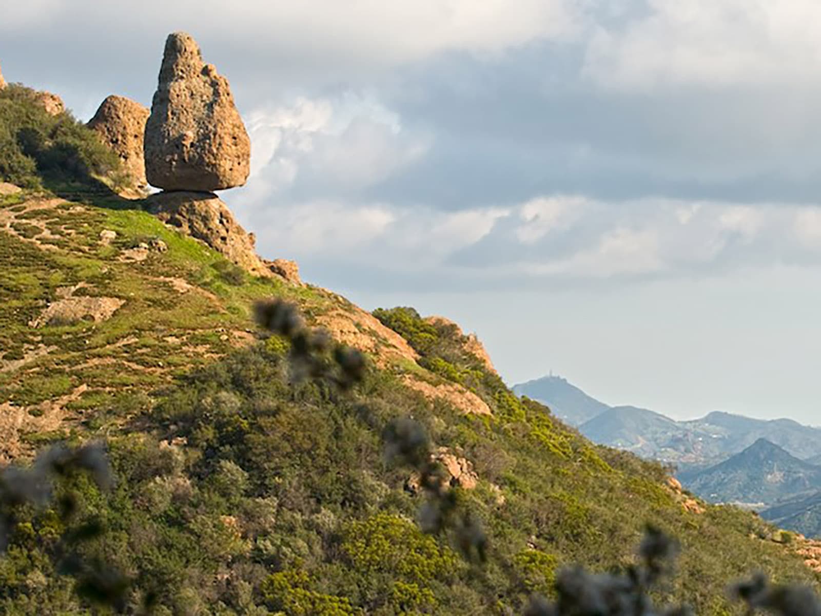 A rock balanced on the side of a mountain.