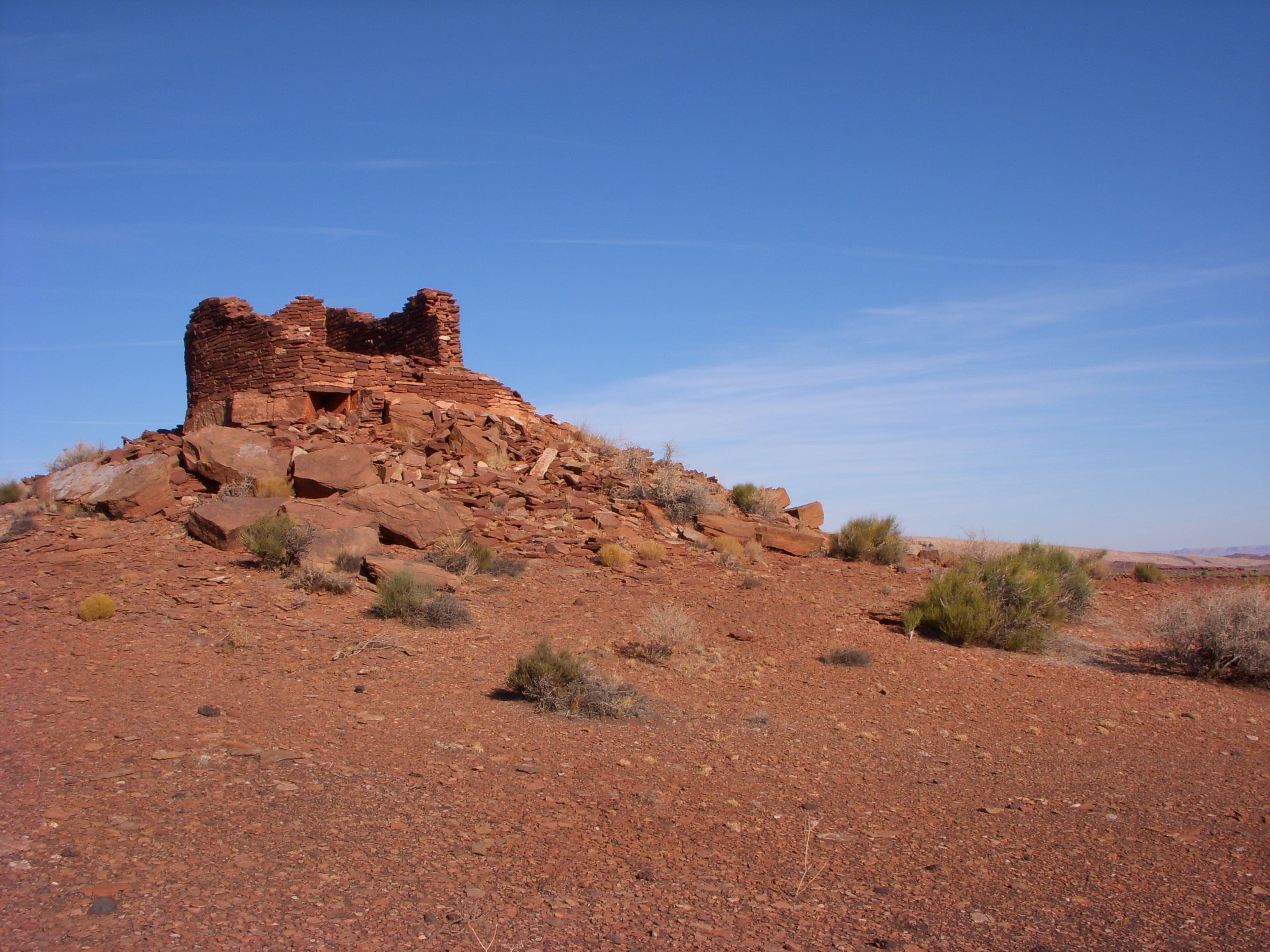 The remains of a small stone pueblo on the top of a small red sandstone hill.