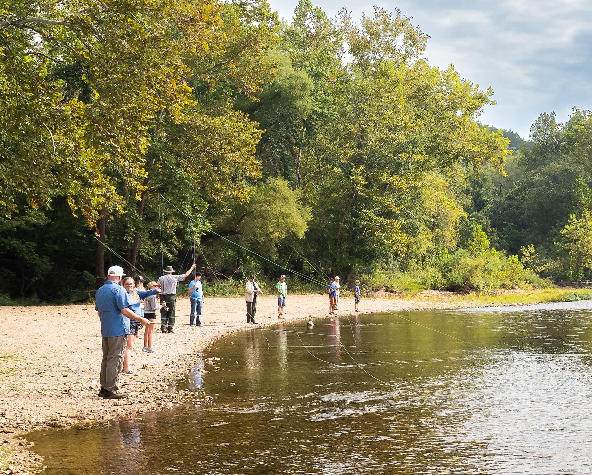 A group of visitors practice casting fly rods along the river's edge.