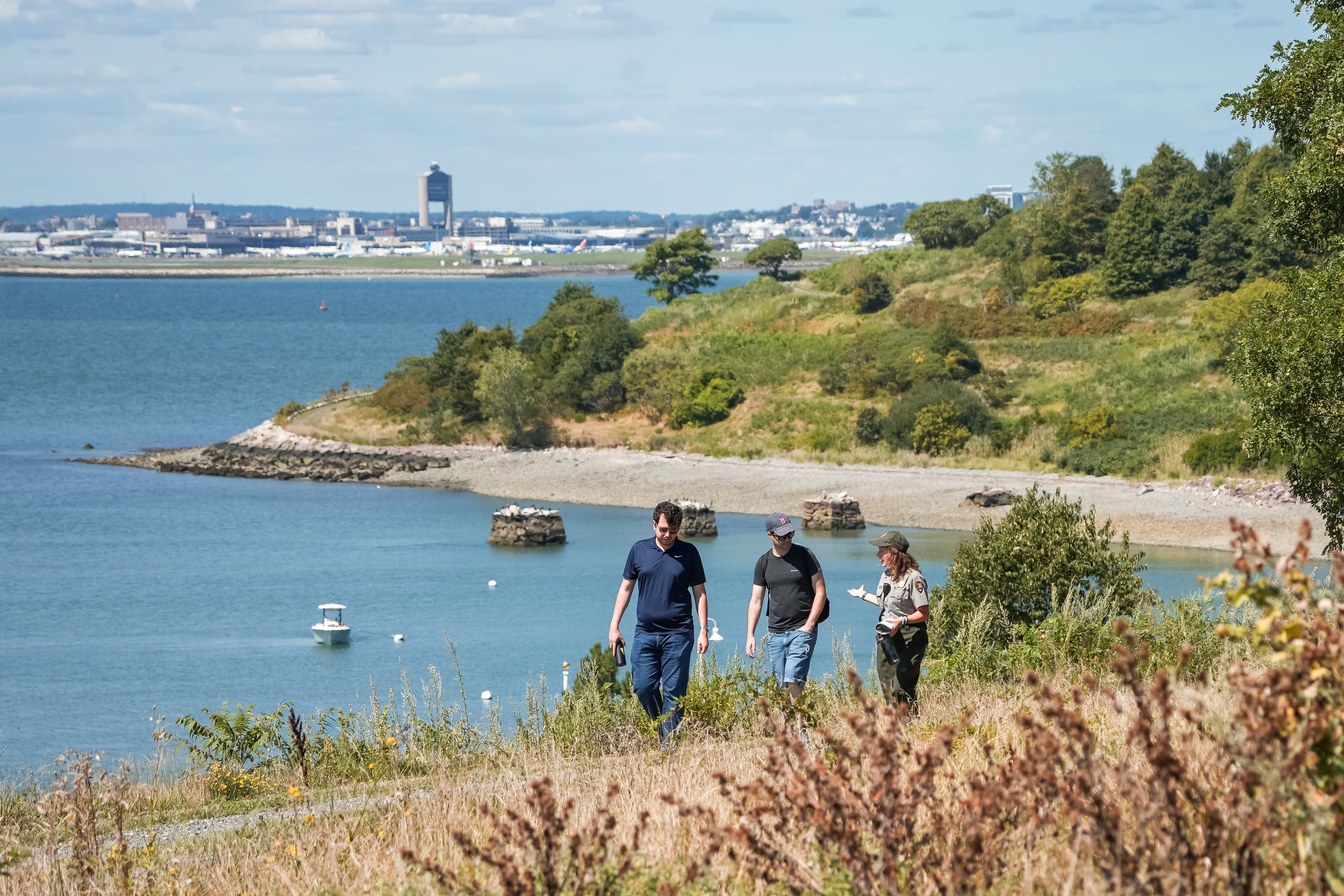 A ranger walks along a gravel path on an island talking to two other people