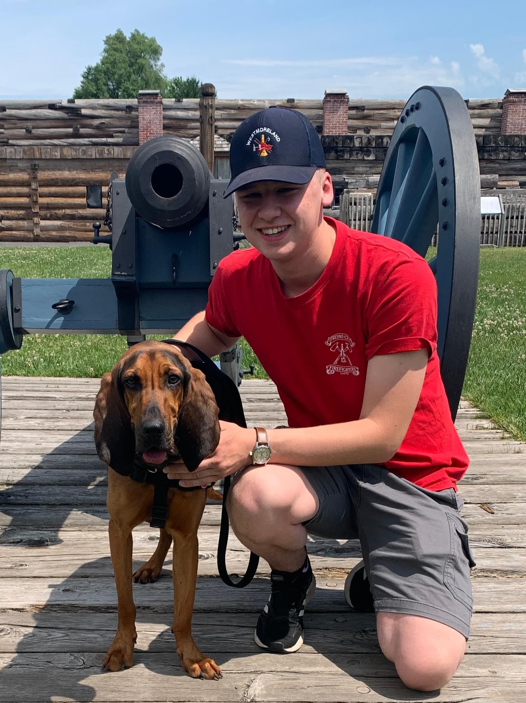 A sweet doggy stands on a leash with his person in front of a cannon.