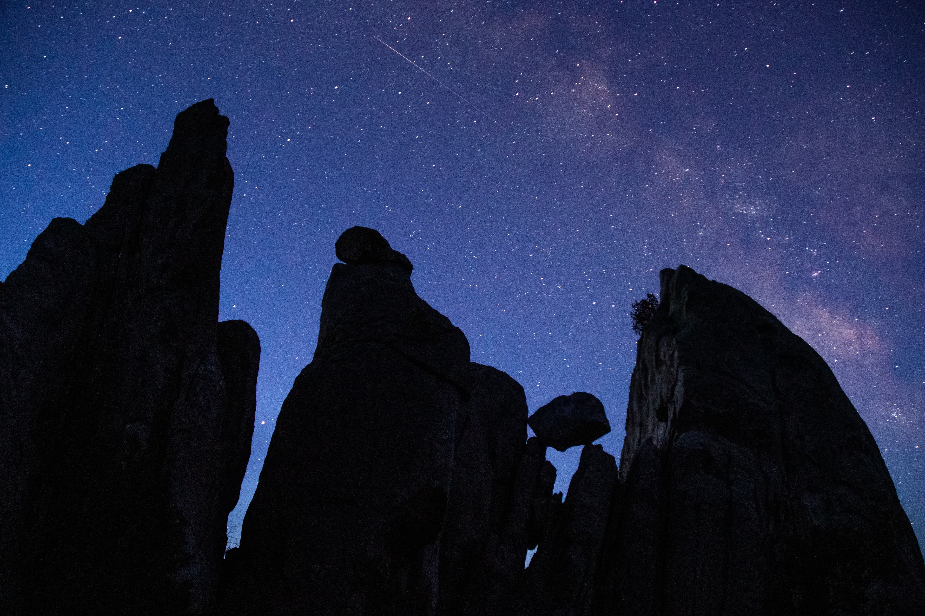 Silhouettes of 3 large pinnacles and a smaller balanced boulder under a purple and blue starry sky.
