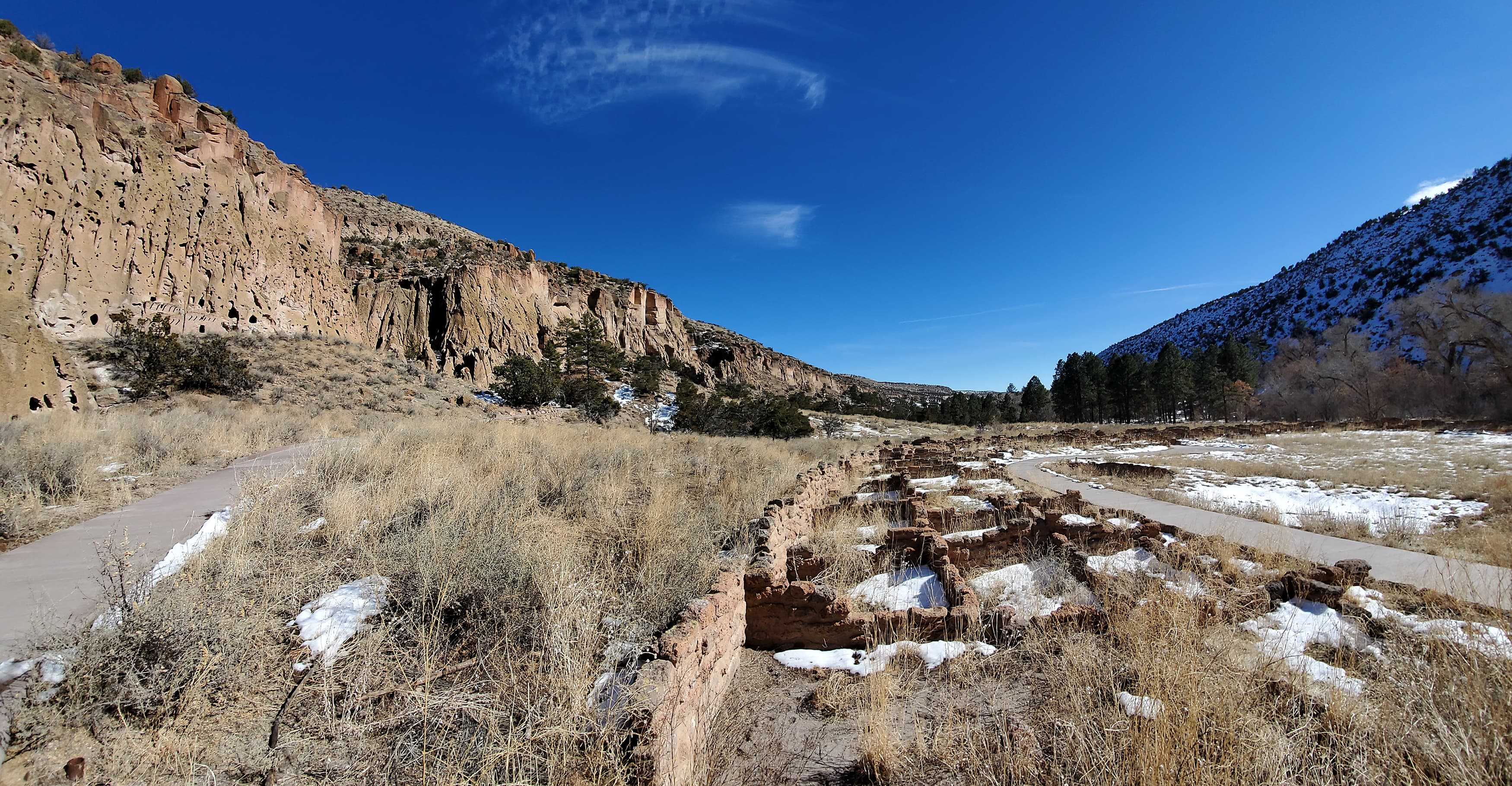 remnants of a stone village in the bottom of a canyon with steep rocky tan cliffs and blue sky