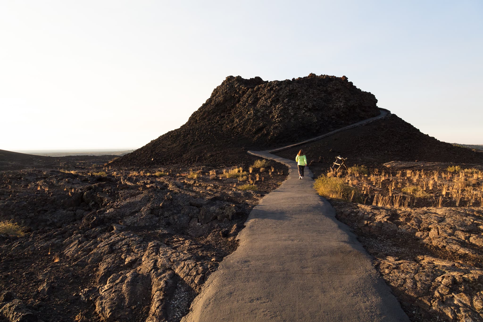 a person walking on a paved path up to a small volcanic cone
