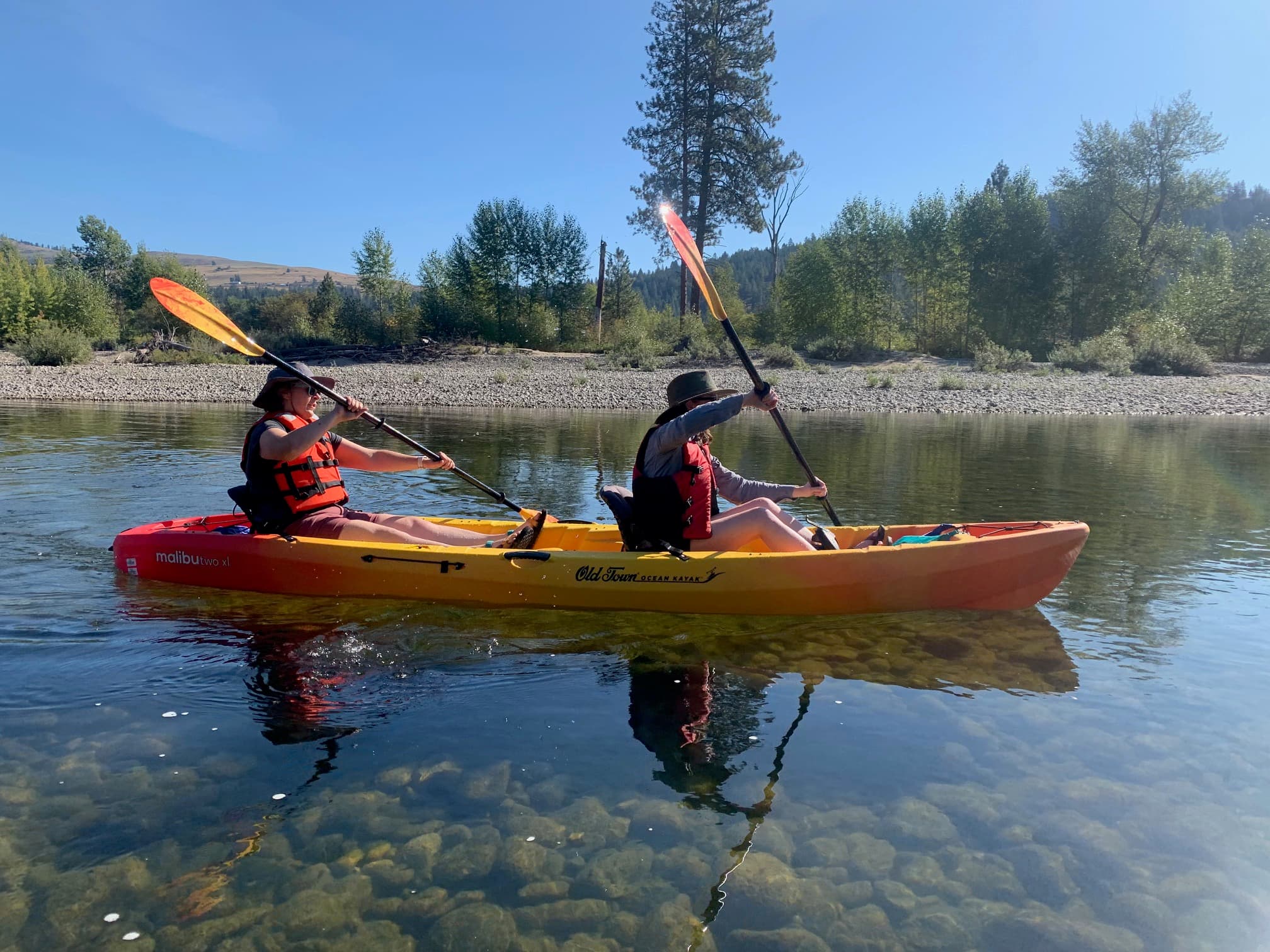 An orange kayak holds two paddlers out on clear shallow water.